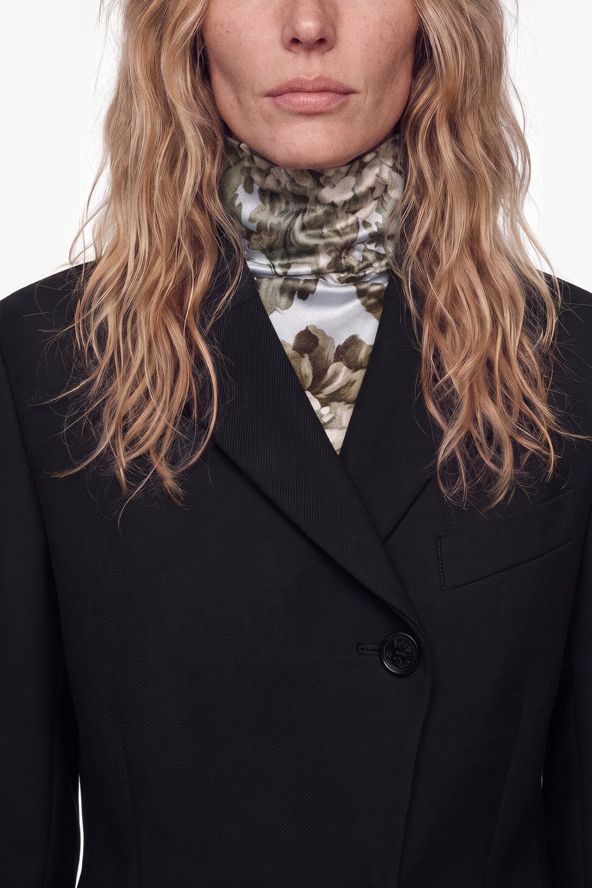 Close-up of tailored black suit jacket with floral turtleneck, model’s face partially visible.