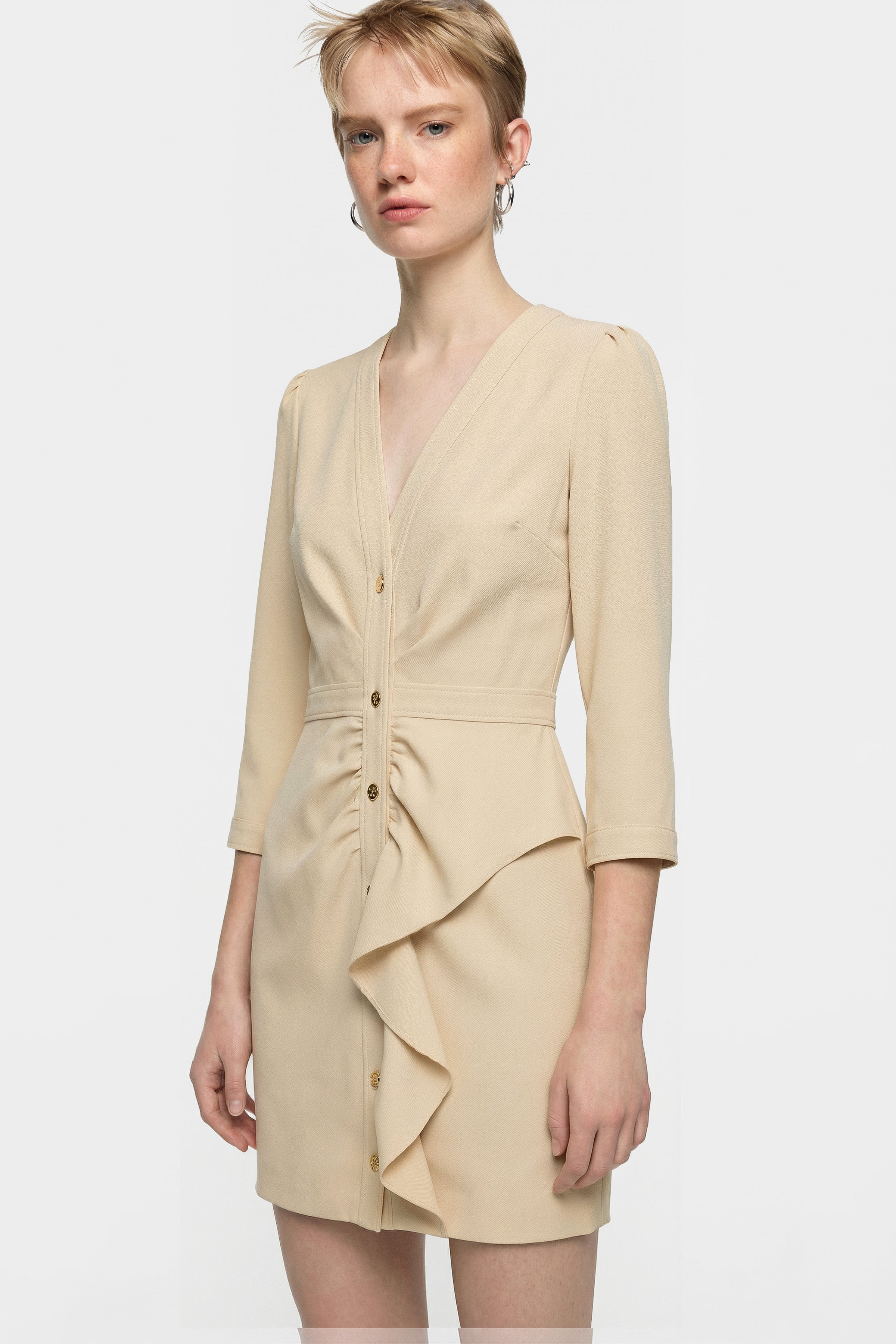 Front view of a model wearing an elegant beige ruffle button dress.