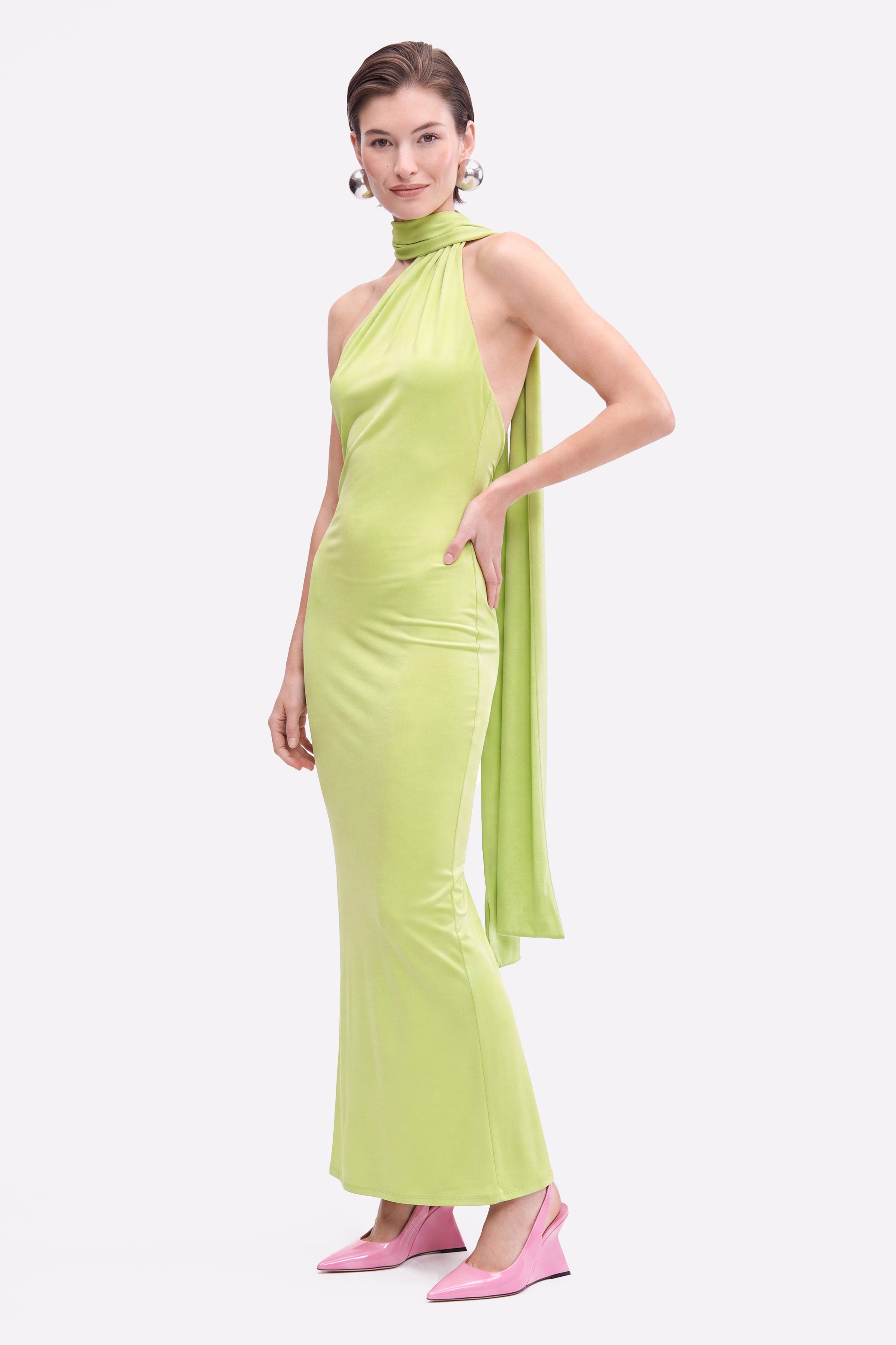 Model in lime asymmetric halter dress with draped back detail, pink shoes.