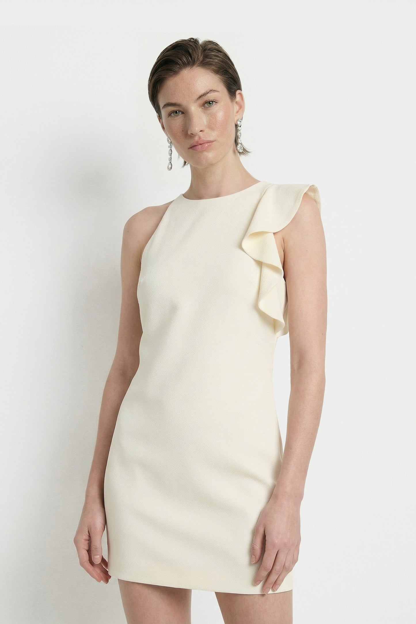 Front view of cream dress with ruffle shoulder detail, model wearing earrings.