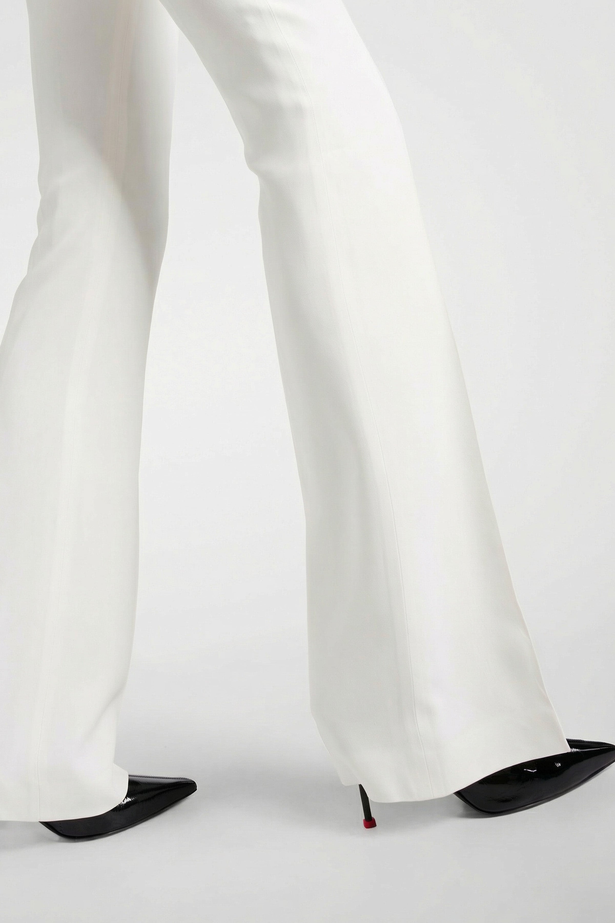 Model wearing ivory tailored flare pants, side view, with black pointed heels.