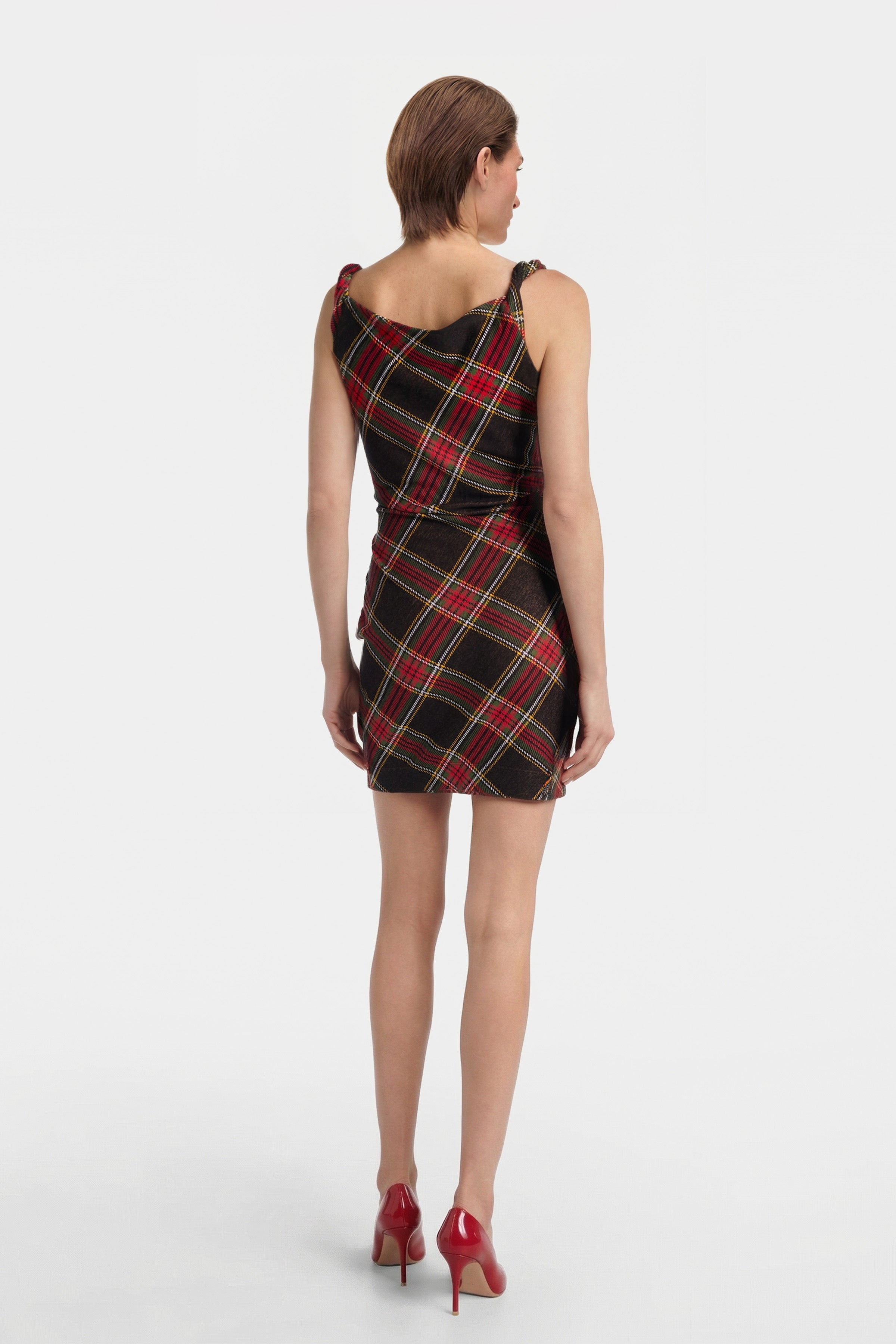 Rear view of model in a draped tartan mini dress and red heels.