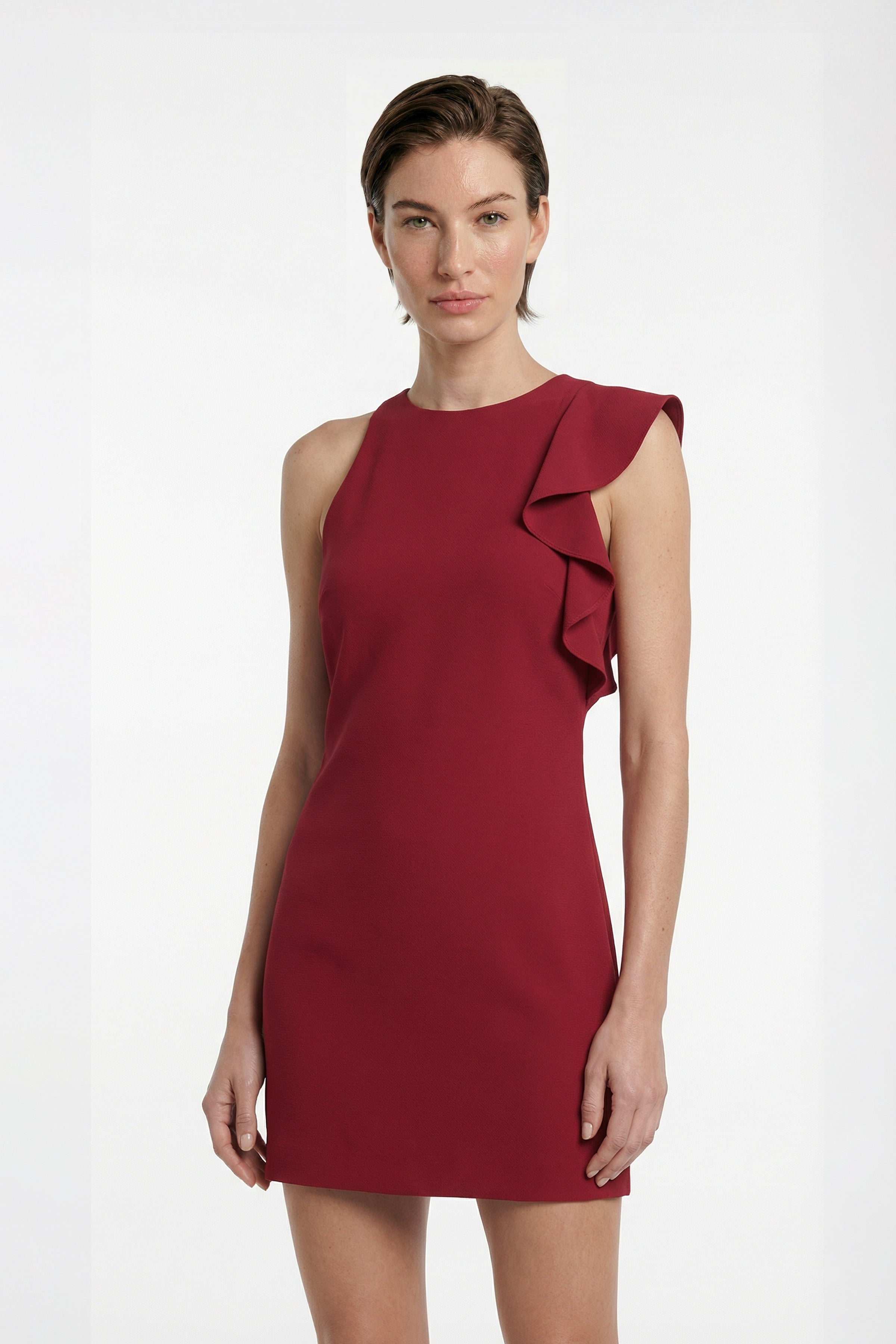 Front view of scarlet mini dress with ruffled shoulder detail. Model's hair short.