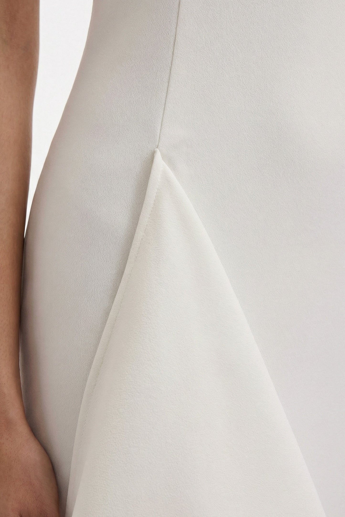 Close-up of asymmetrical white dress fabric detail, showing texture and design.