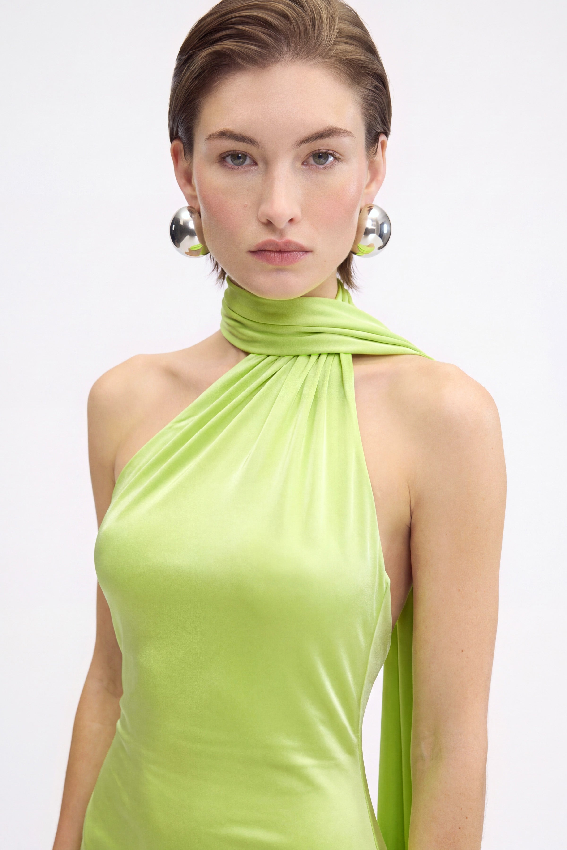 Model wearing a lime-green asymmetric halter dress with metallic earrings, front view.