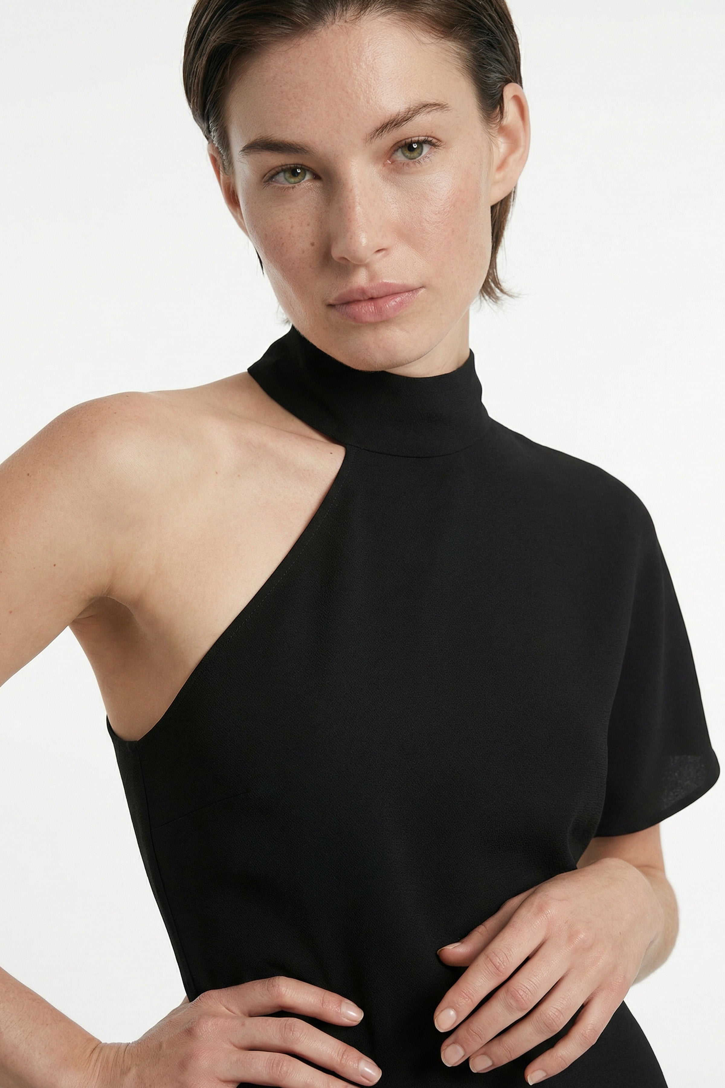 Model wearing asymmetrical black midi dress with high neck, showing front view detail.