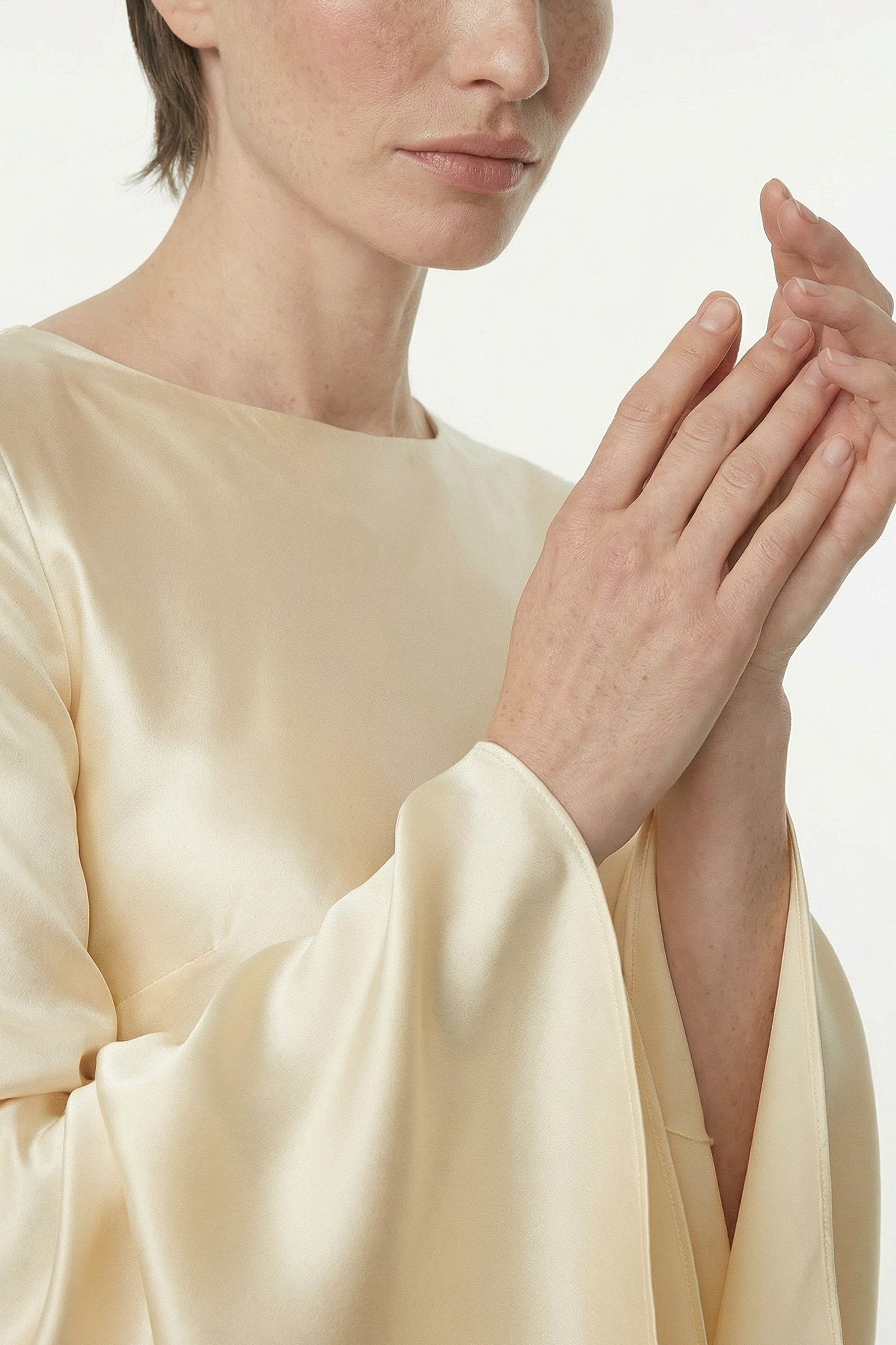 Close-up of model in golden silk gown, highlighting smooth fabric and elegant sleeves.