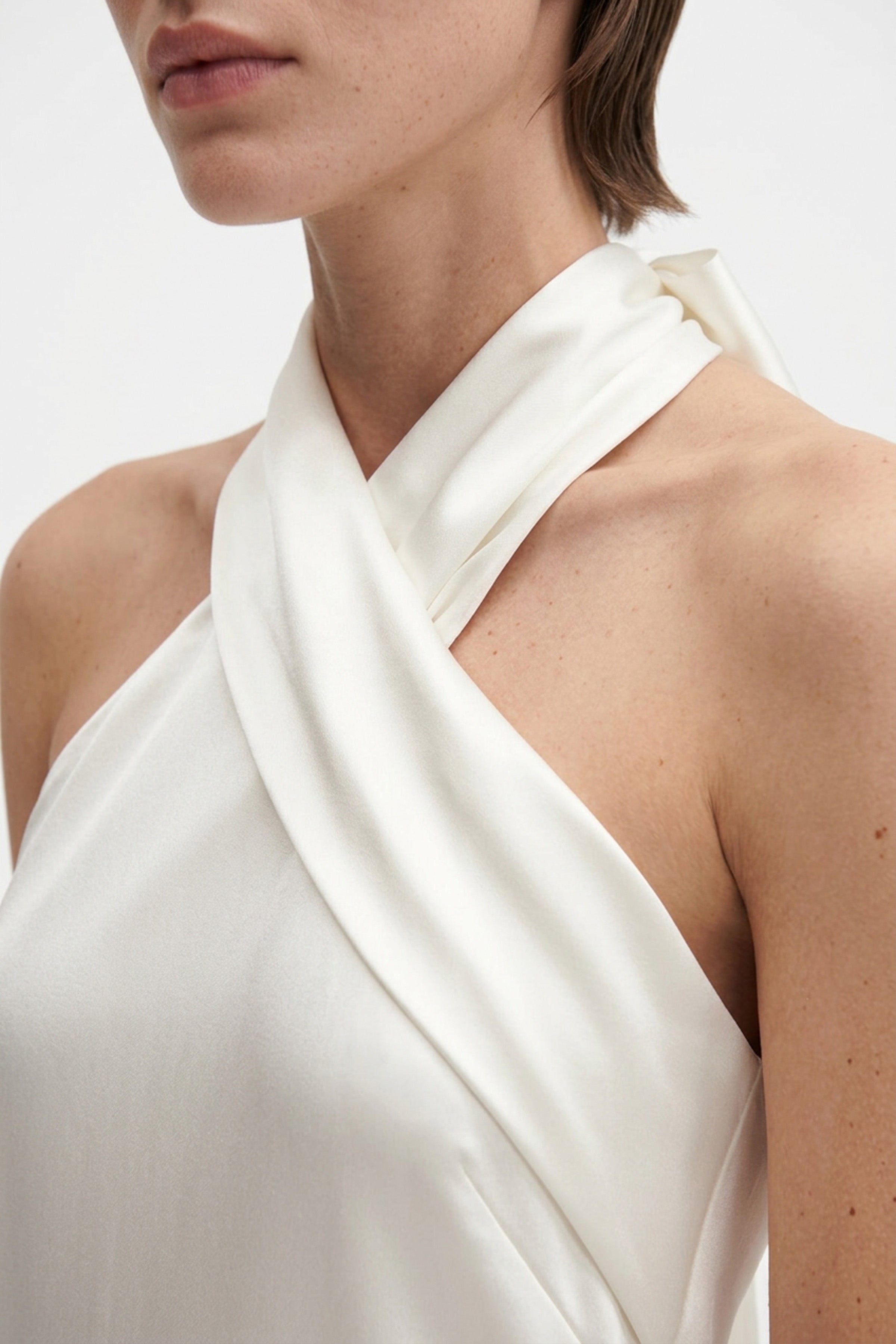 Close-up of white silk halter gown neckline, showcasing smooth fabric and elegant design.