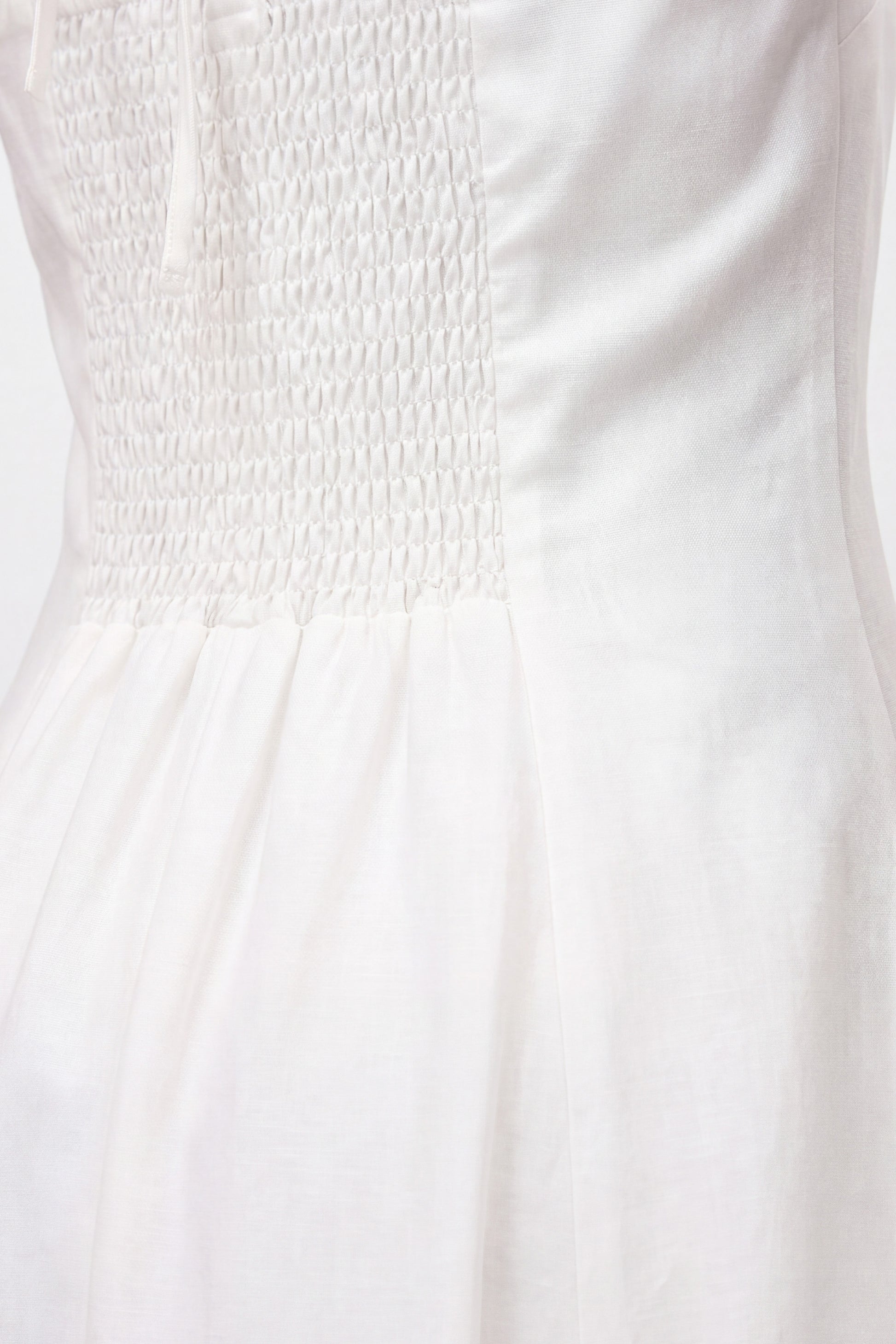 Close-up of white halter midi dress with smocked bodice and soft fabric detailing.