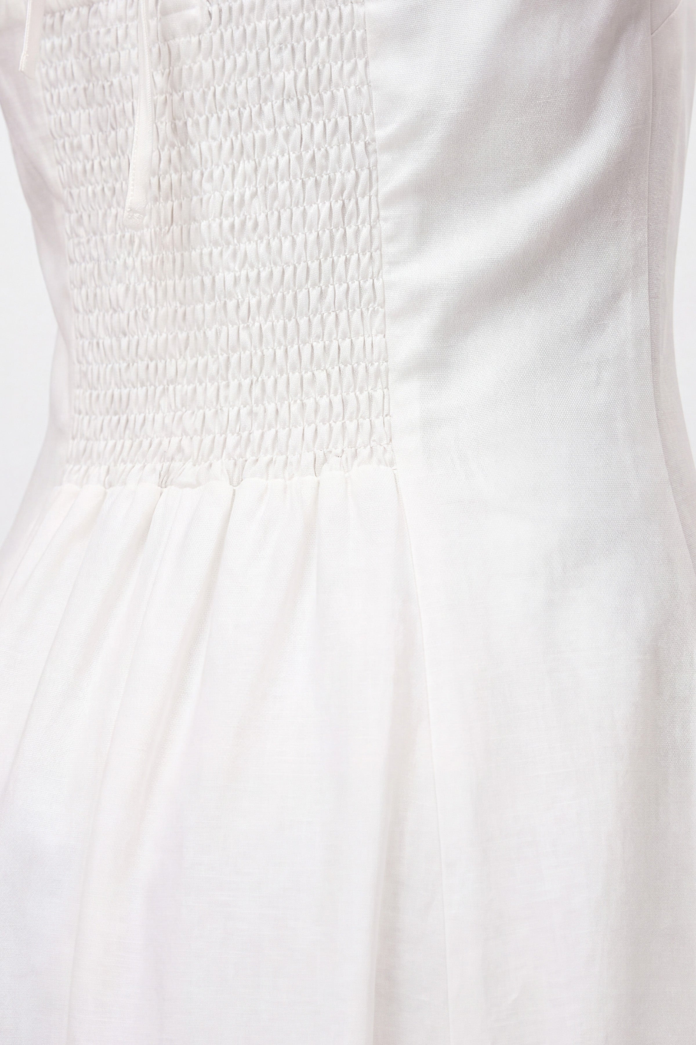 Close-up of white halter midi dress with smocked bodice and soft fabric detailing.