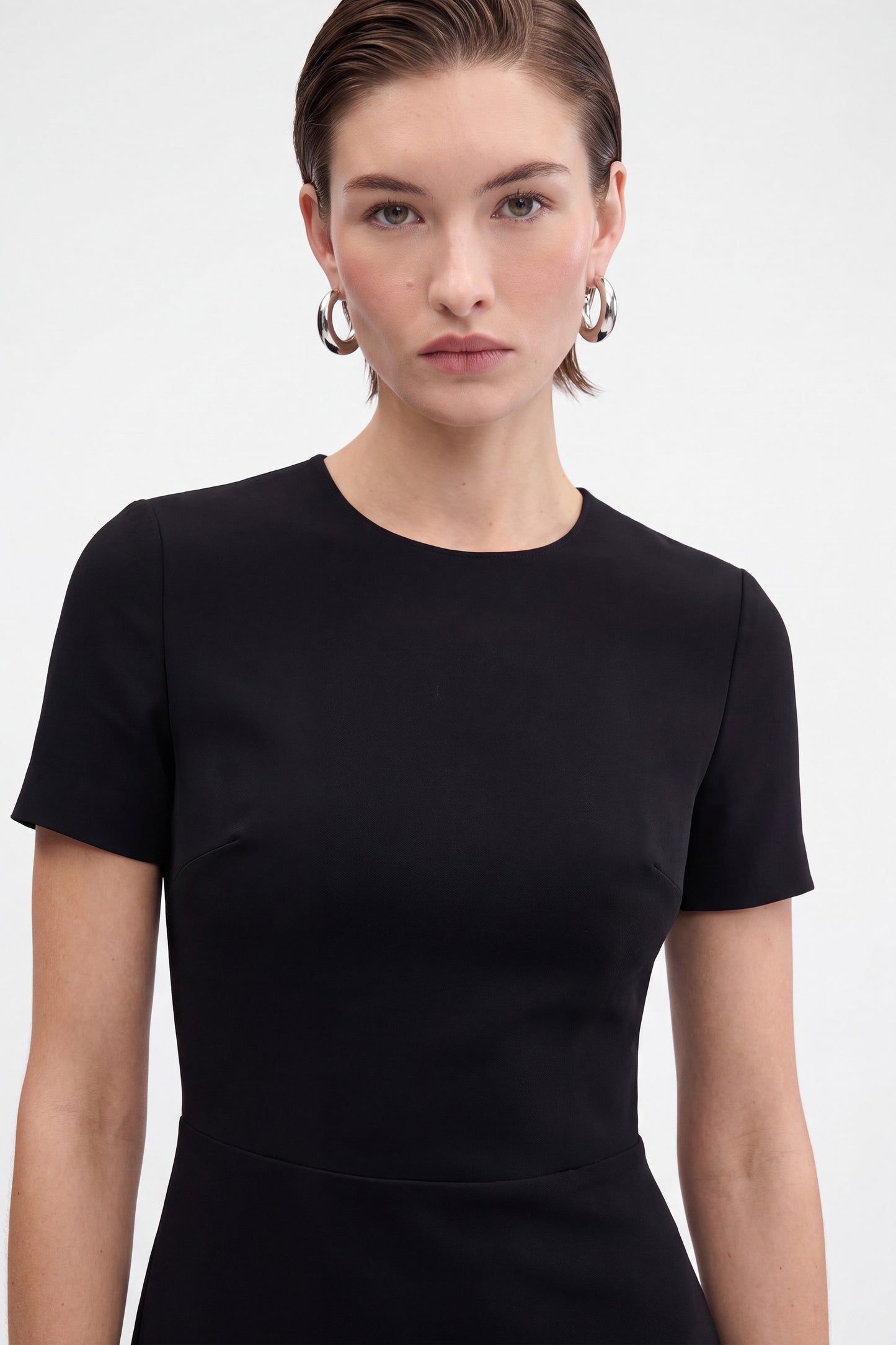 Front view of black ruffle hem dress, model wearing silver hoop earrings.