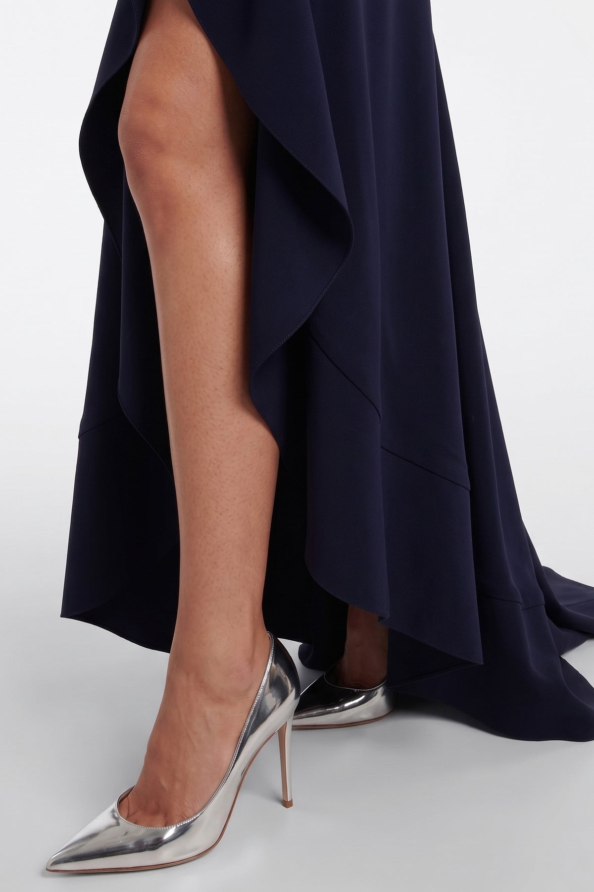 Navy ruffle hem gown detail, silver heels, model's legs, elegant evening look.