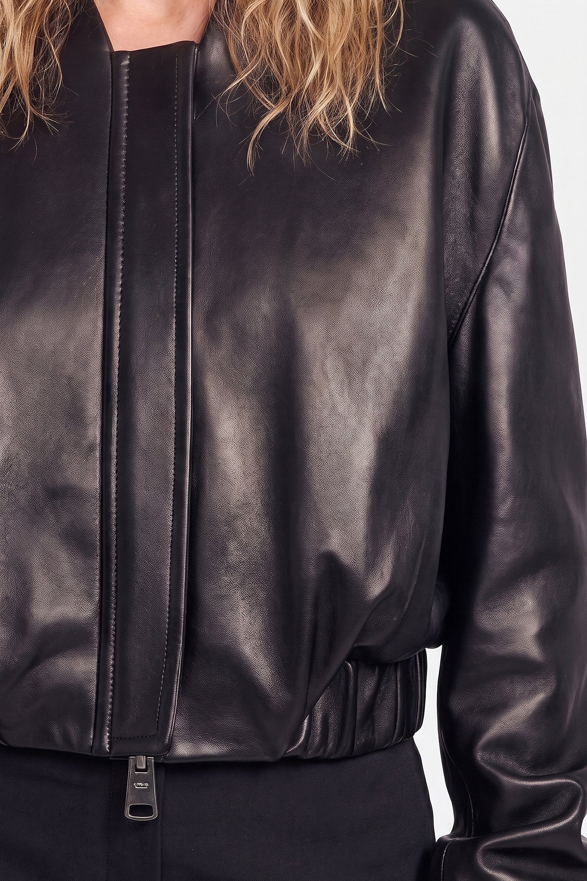 Close-up of black leather bomber jacket front with zipper detail, worn by model.