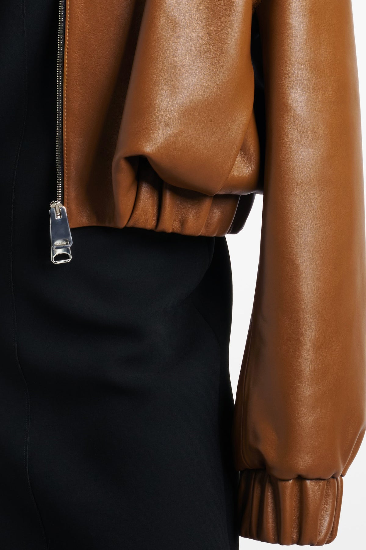 Close-up of cognac leather bomber jacket sleeve with zipper detail and elastic cuff.