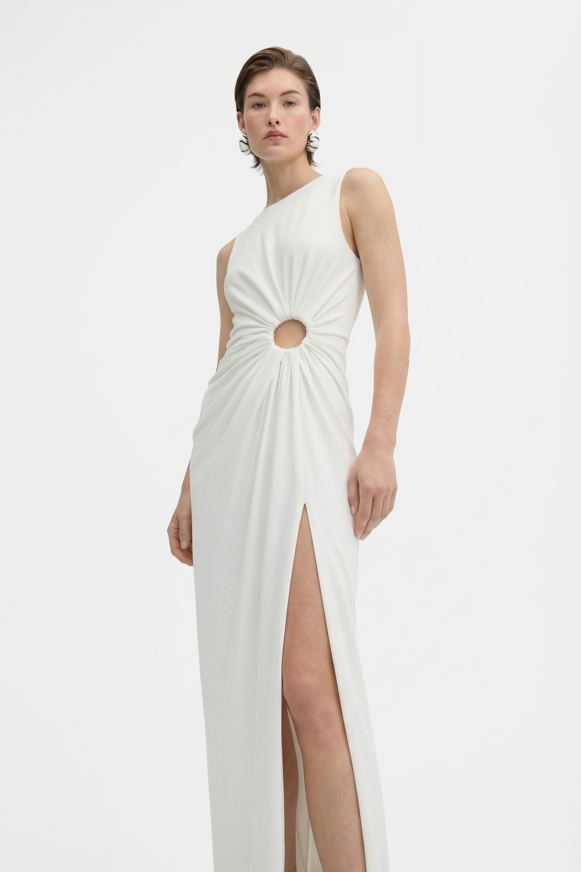 Front view of model wearing a white gown with cut-out and thigh-high slit.