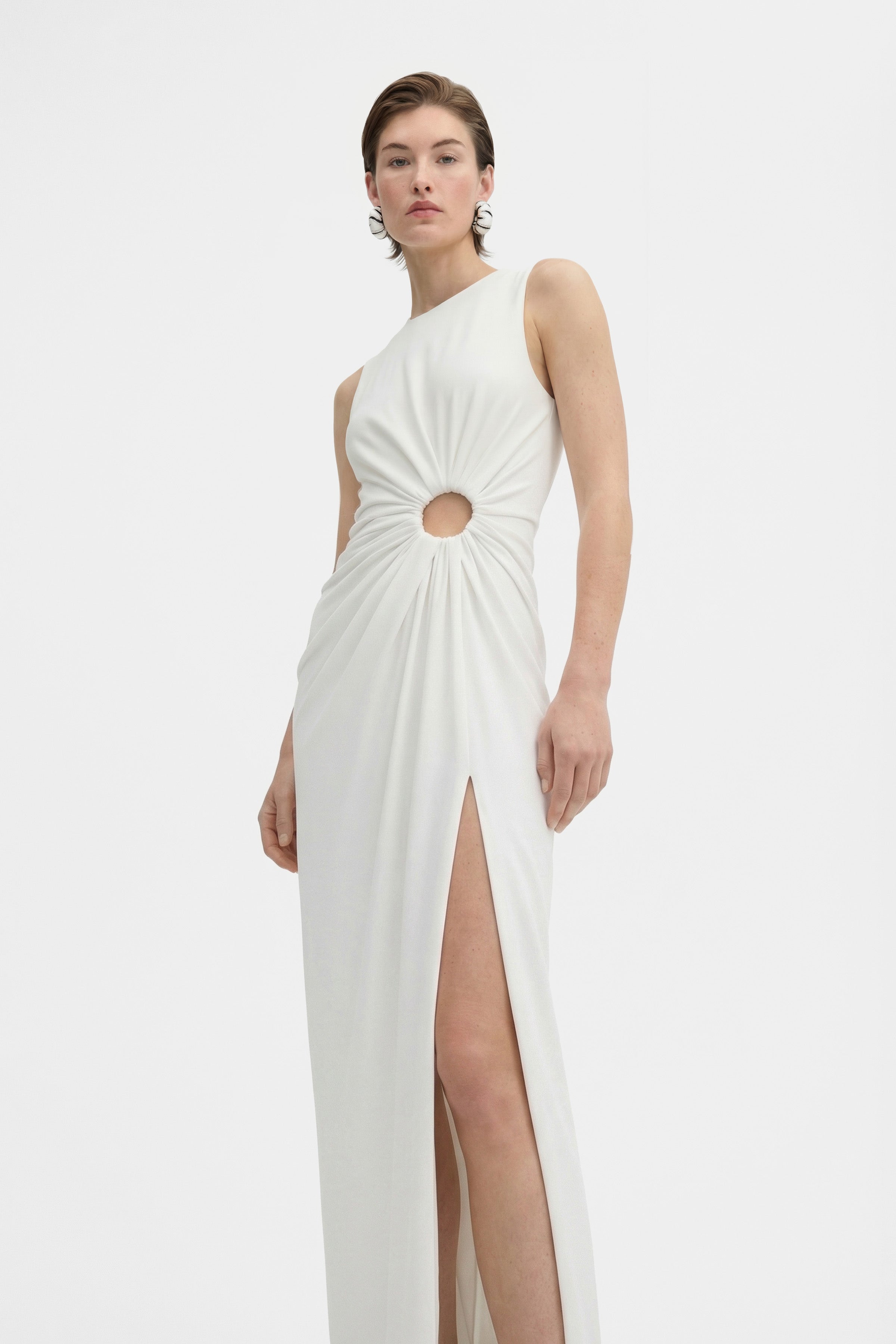 Front view of model wearing a white gown with cut-out and thigh-high slit.