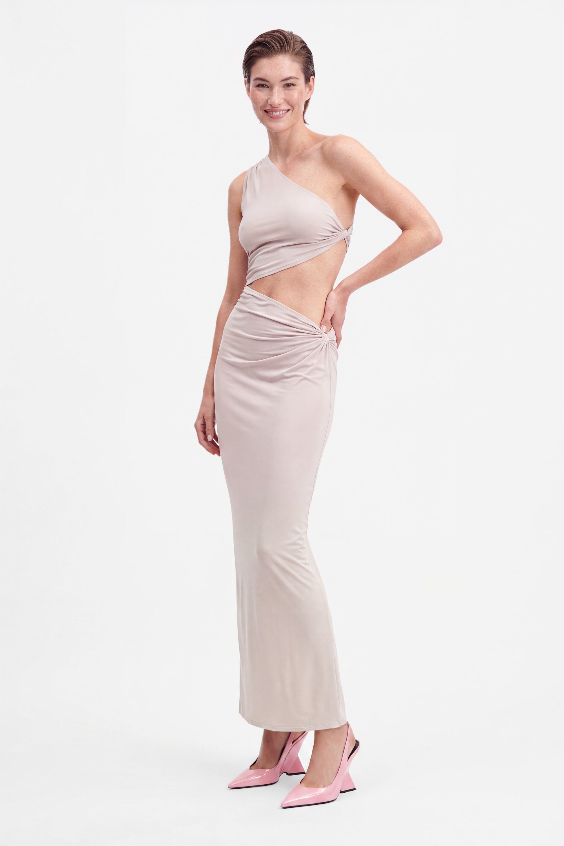 Model in beige asymmetric cutout maxi dress, front view, paired with pink heels.