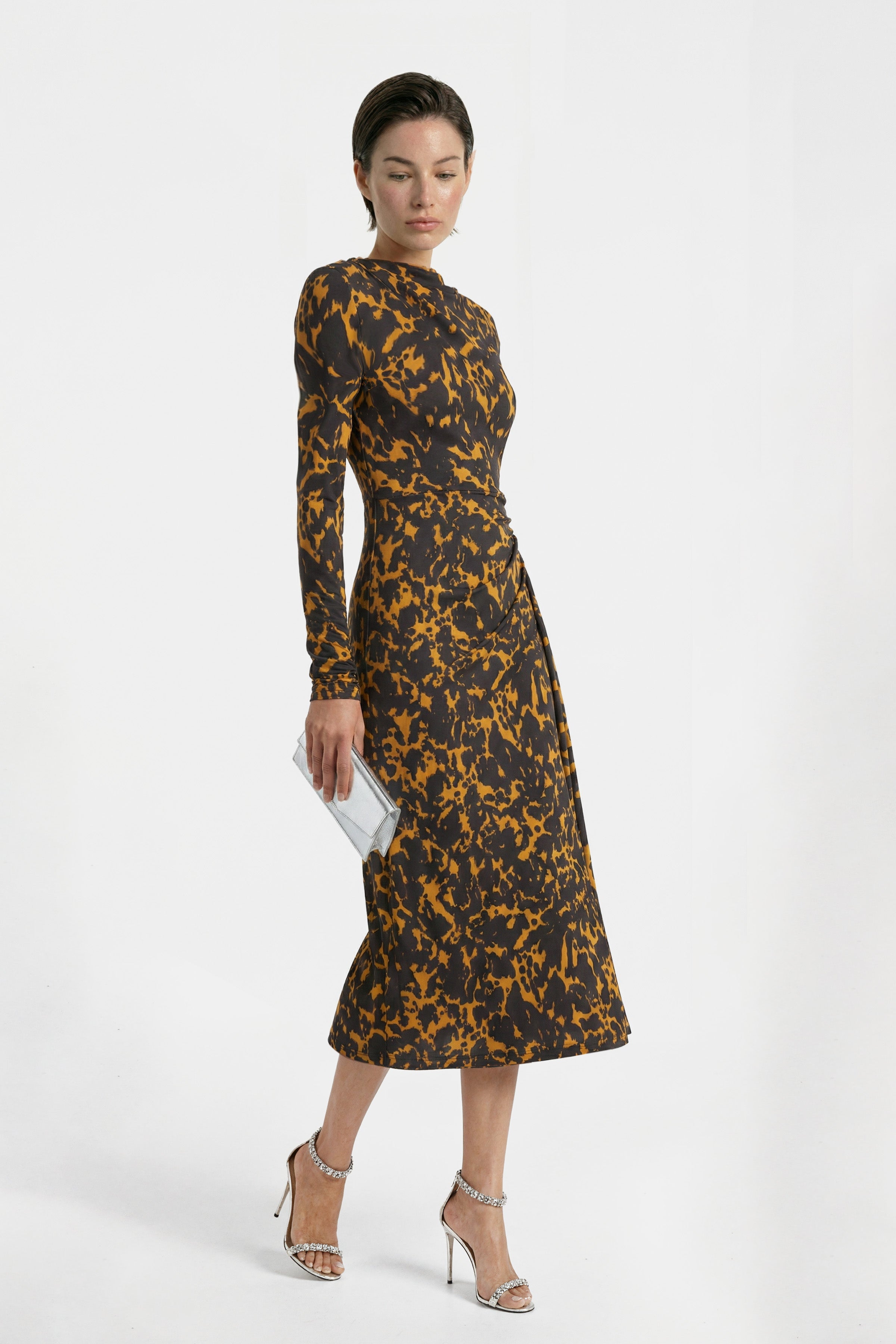 Full-body studio view of a model in a black and gold patterned long-sleeve midi dress with silver heels, gala guest outfit inspiration.