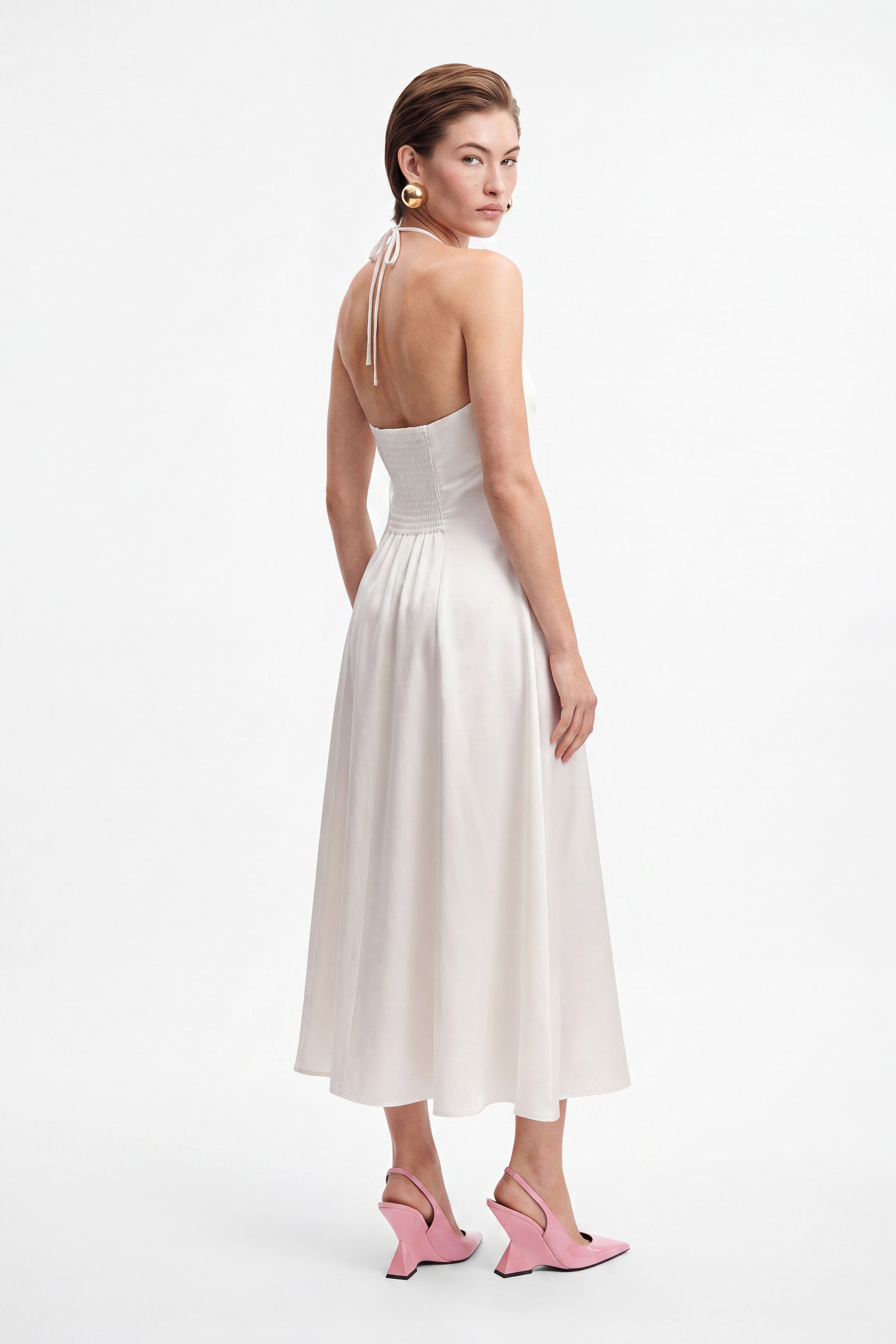Back view of a white halter midi dress with pink heels.