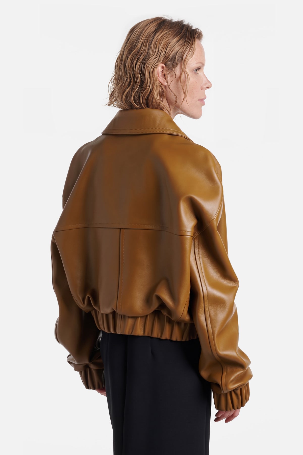 Back view of cognac leather bomber jacket on model, relaxed fit, glossy finish.