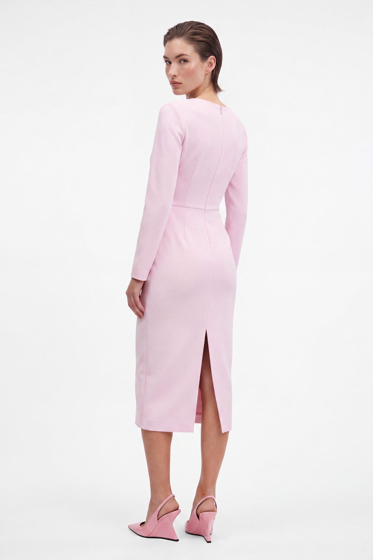Back view of model in soft pink asymmetrical dress with slit and matching heels.