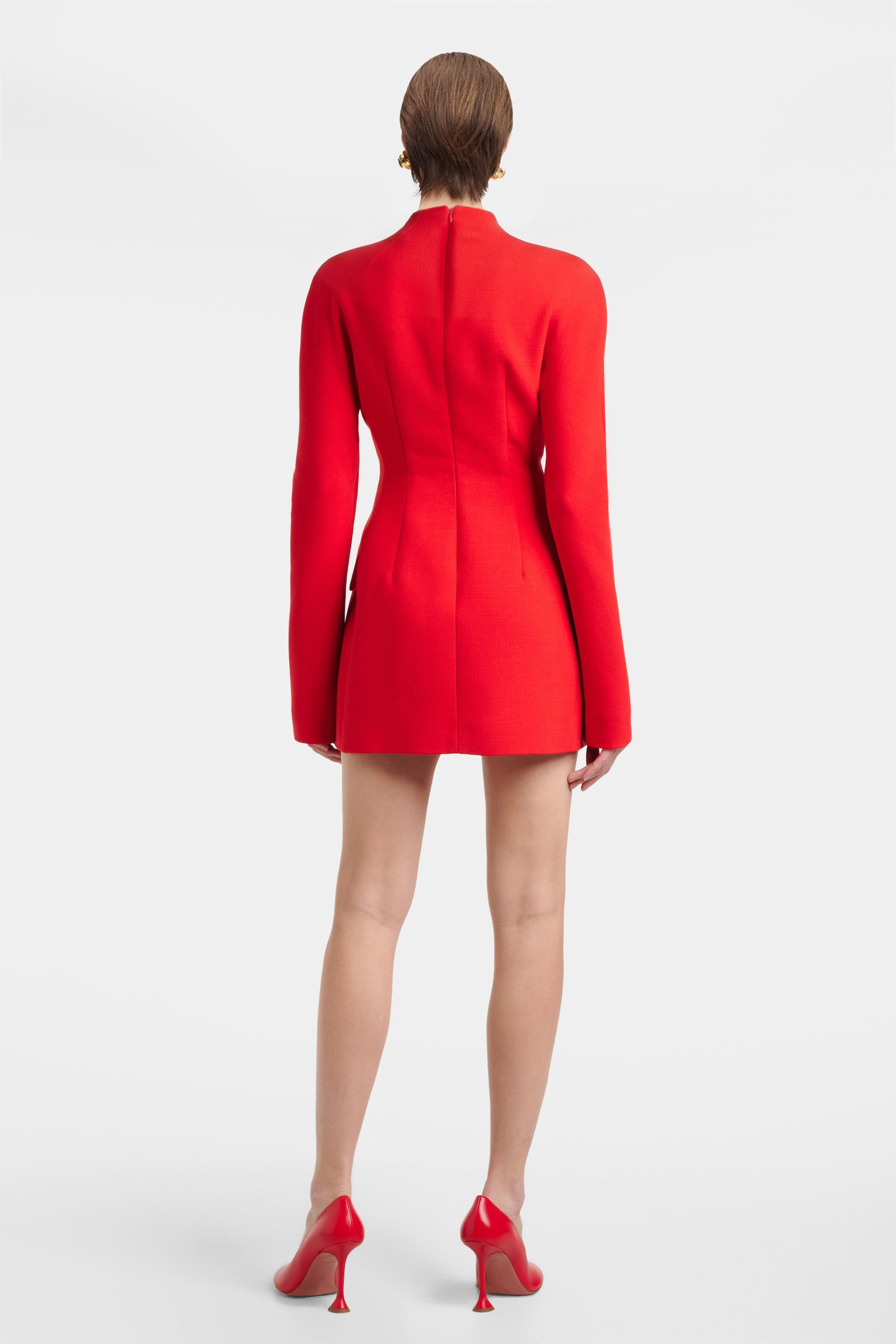 Back view of model in red structured mini dress and matching heels.