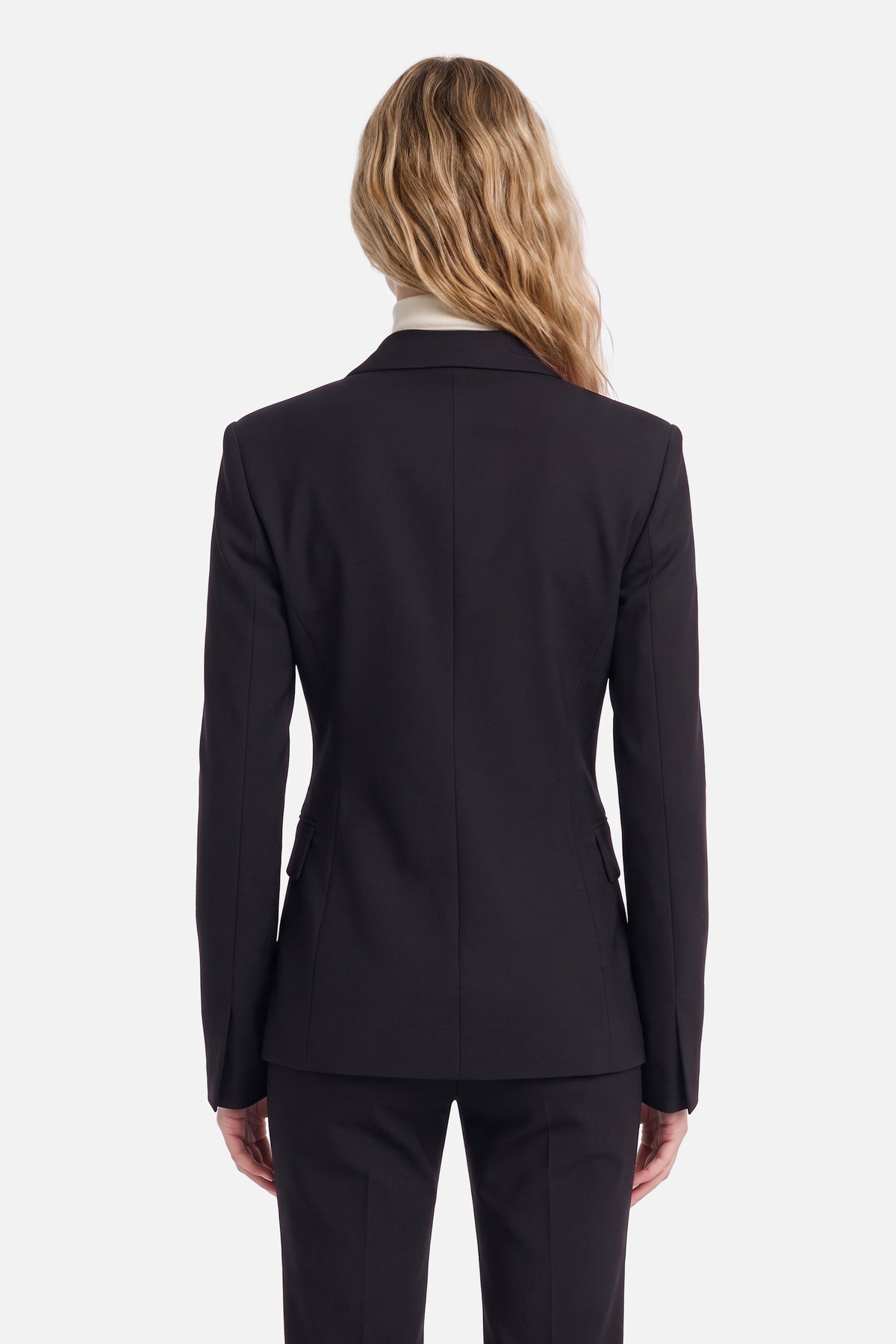 Back view of tailored black suit on model, long blonde hair, white background.