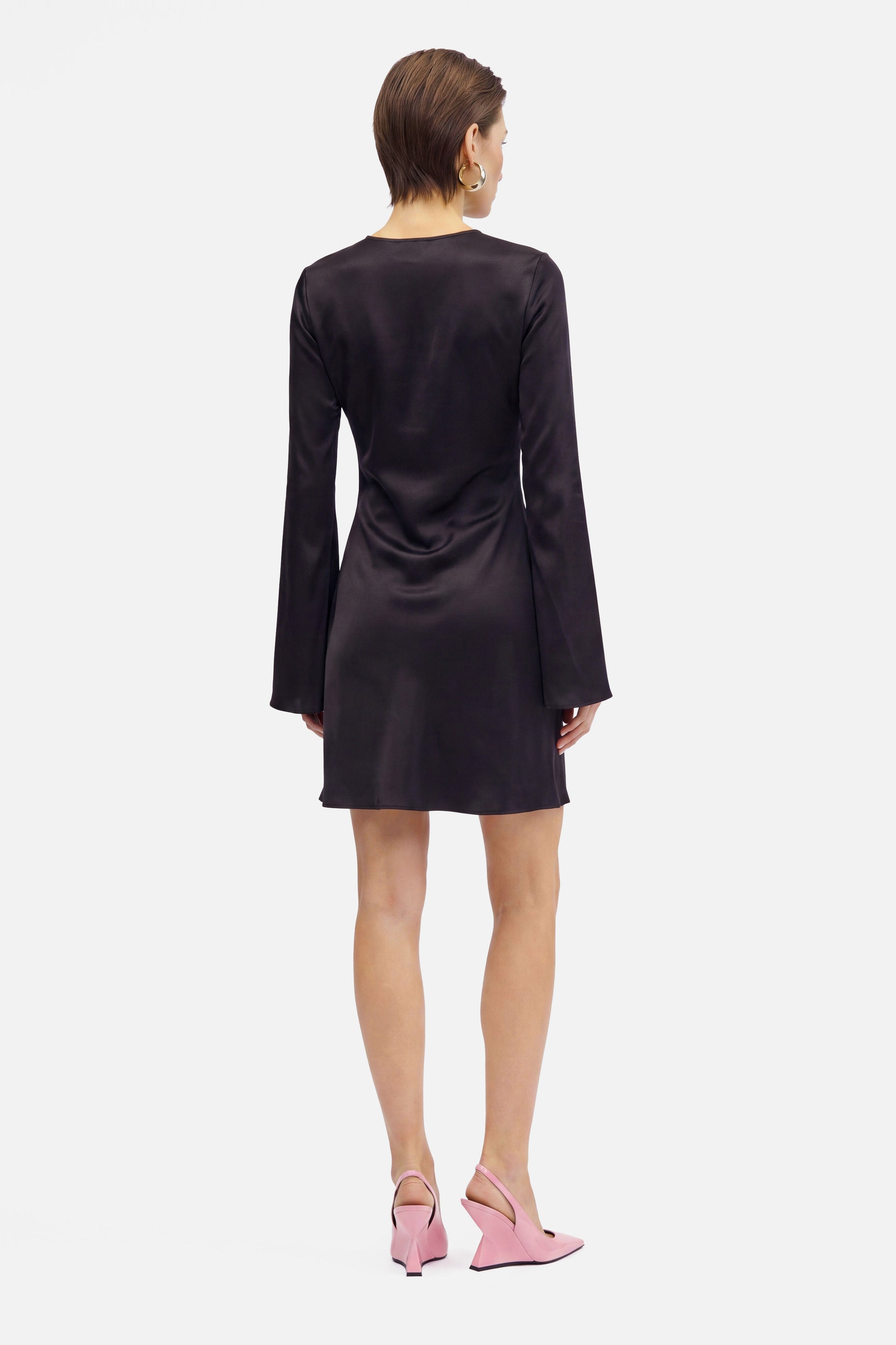 Back view of black satin flare sleeve dress, model wearing pink heels.