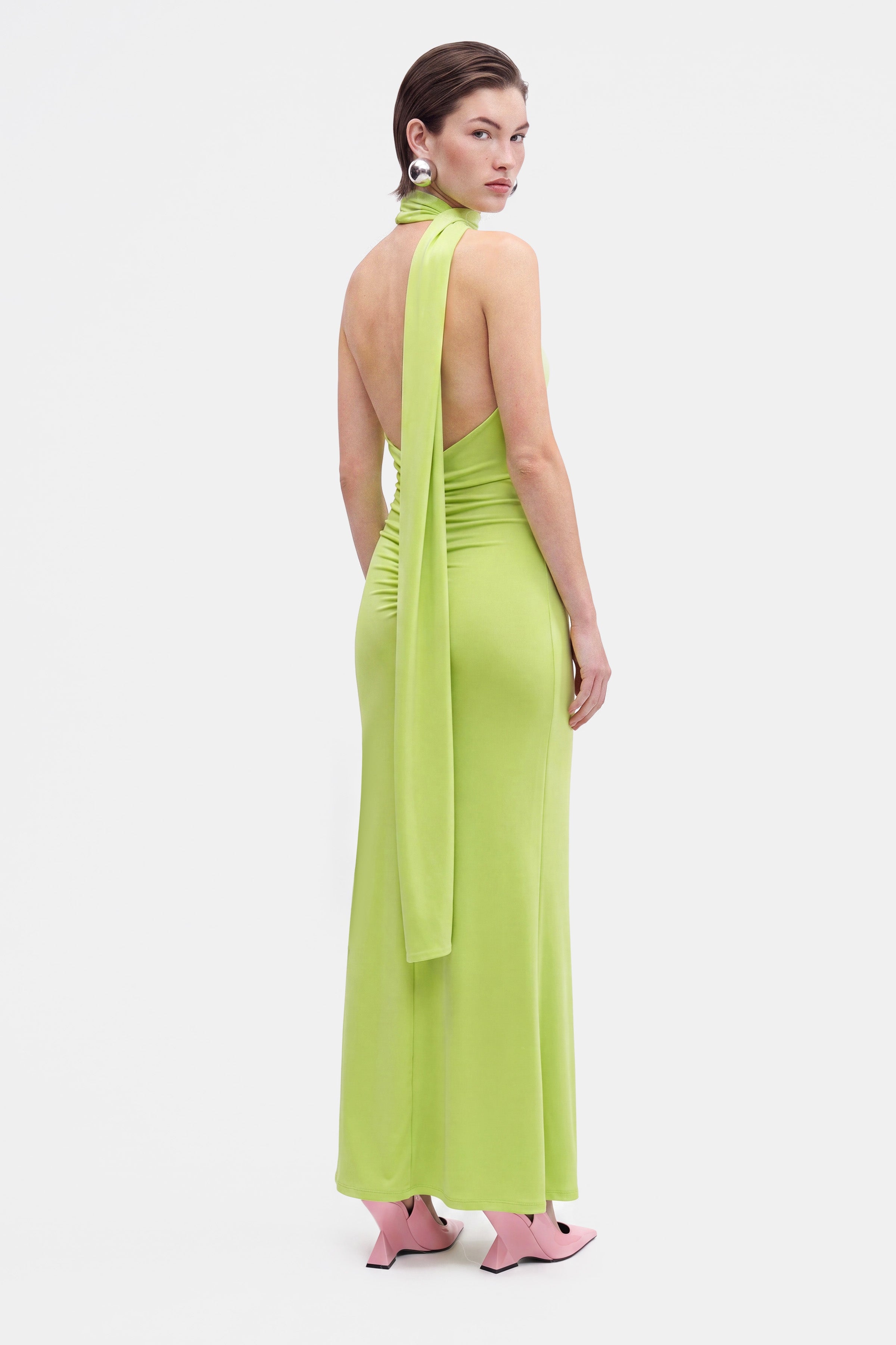 Back view of lime asymmetrical halter dress with long sash detail and pink heels.