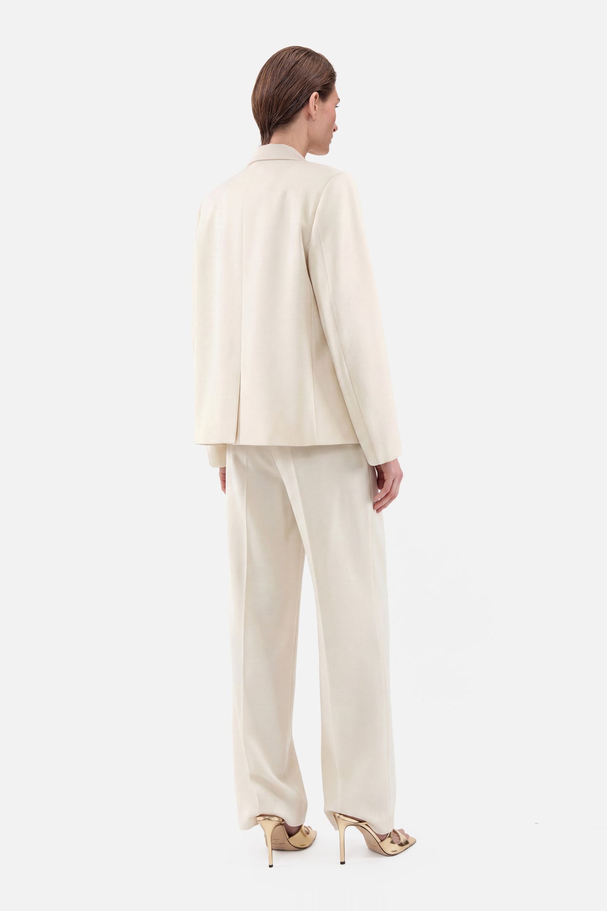 Back view of ivory tailored suit worn with gold high heels.