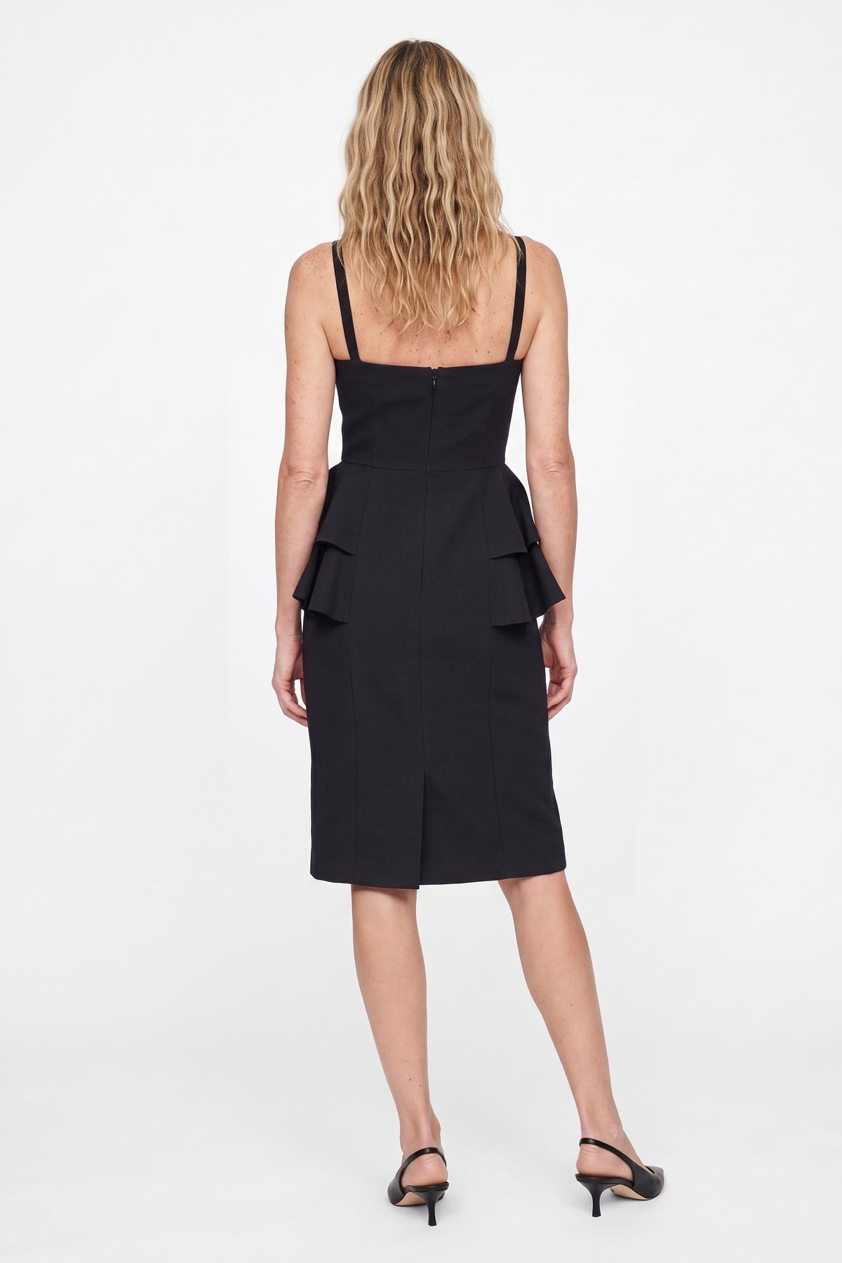 Back view of black sweetheart neckline dress with ruffle details, model standing.