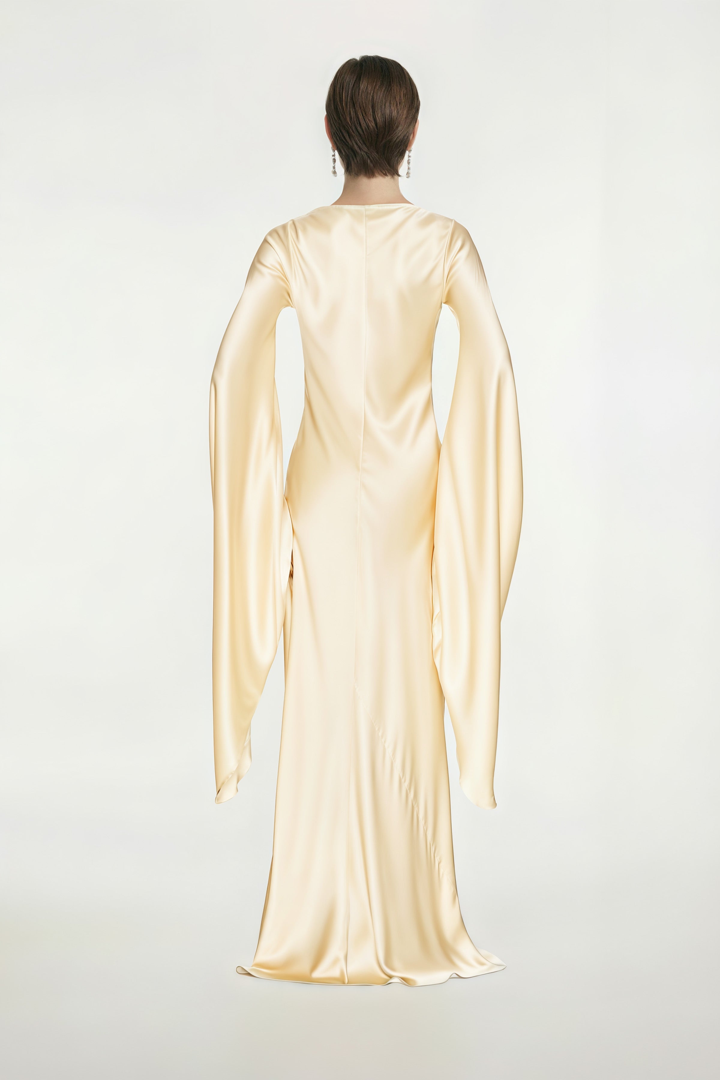 Back view of golden silk gown with draped long sleeves on model.