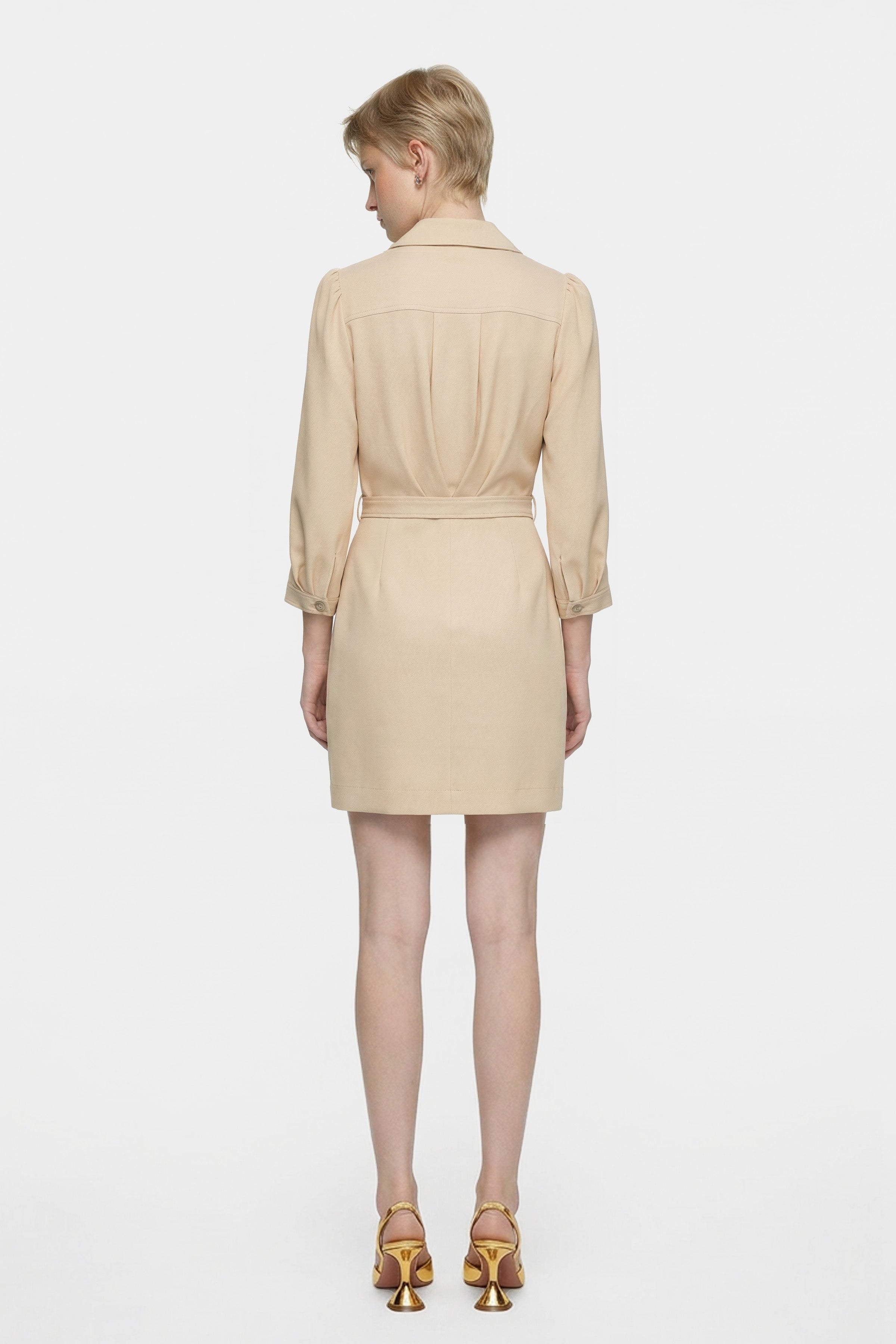 Back view of beige ruffle button dress, model standing in gold heels.