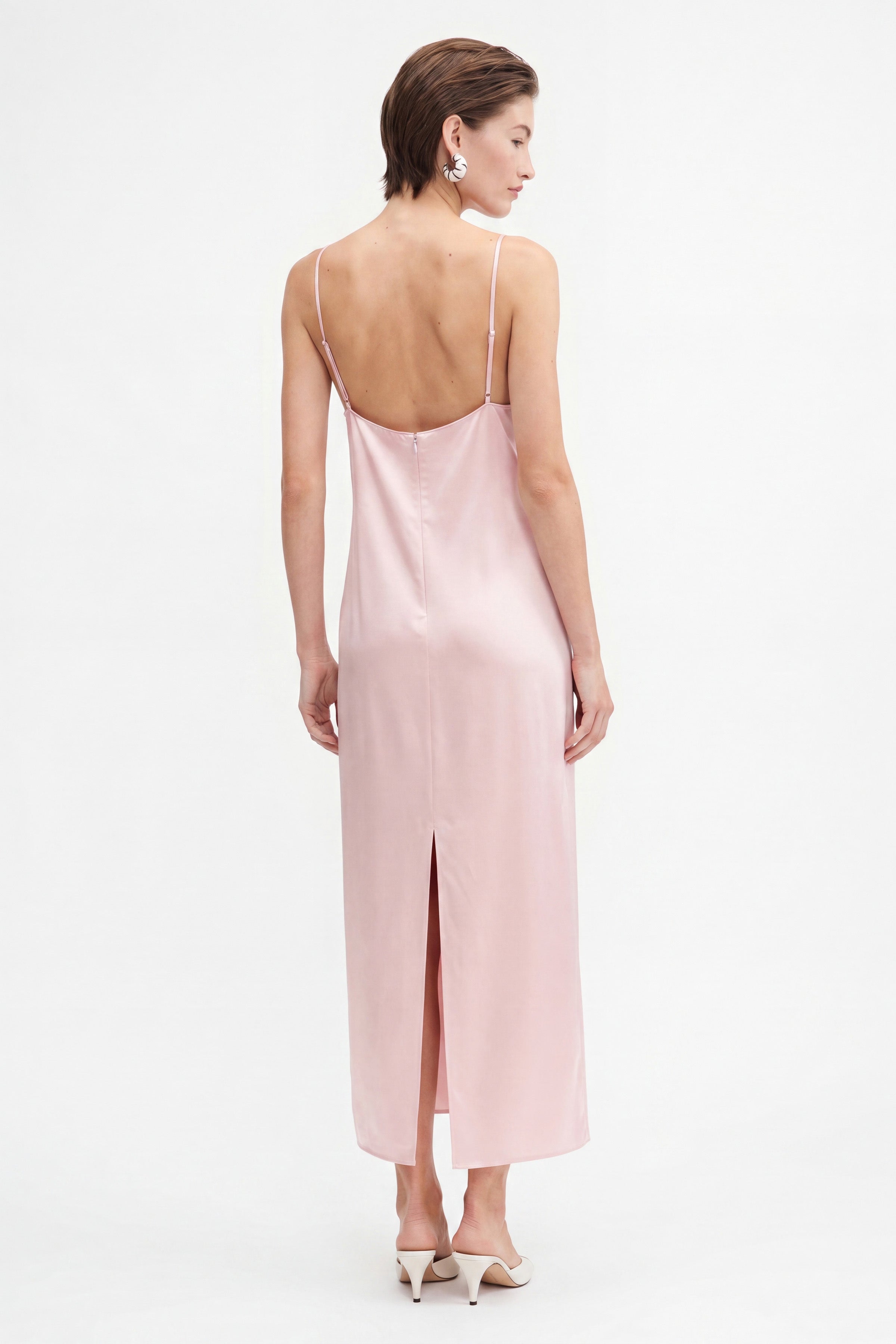 Model wearing blush lace slip dress, back view, spaghetti straps, delicate earrings.