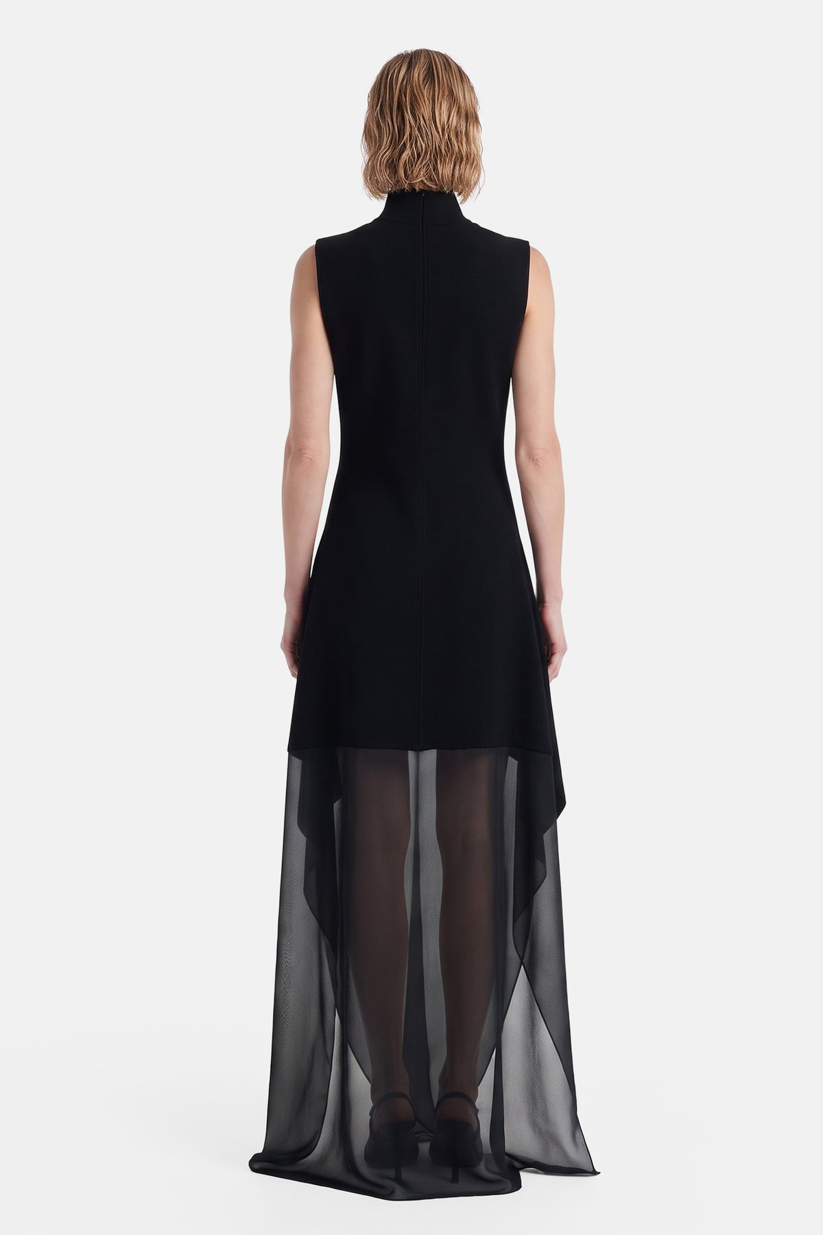 Back view of model wearing black dress with sheer overlay, elegant and flowing.