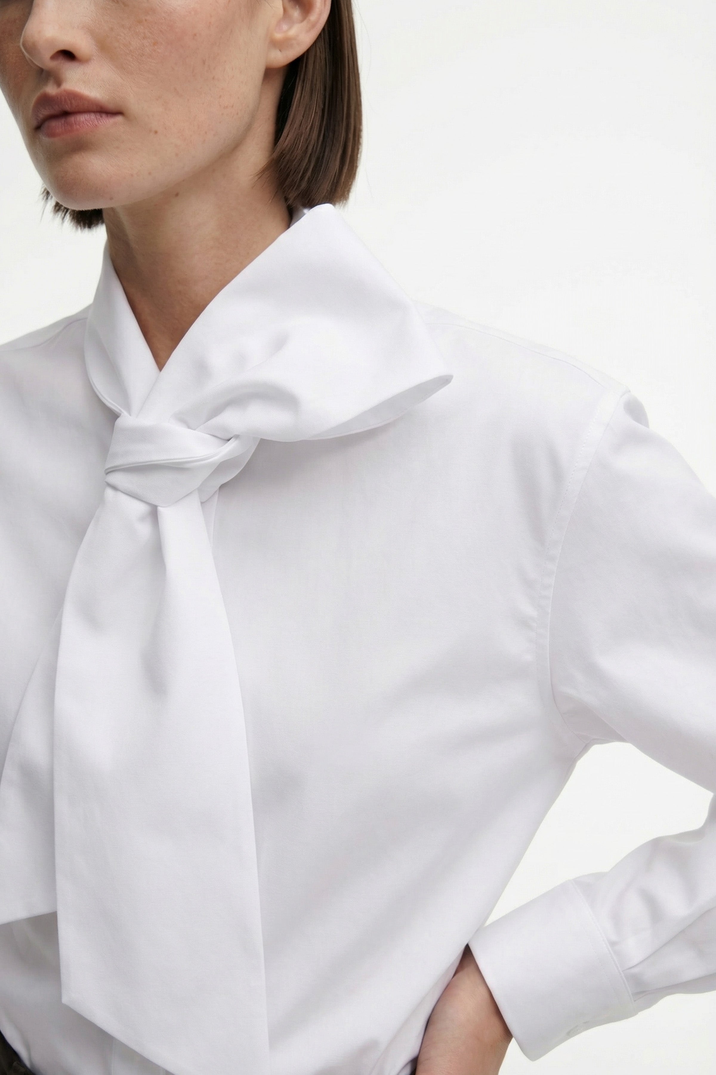Close-up of elegant white blouse with large bow, model wearing it cropped.