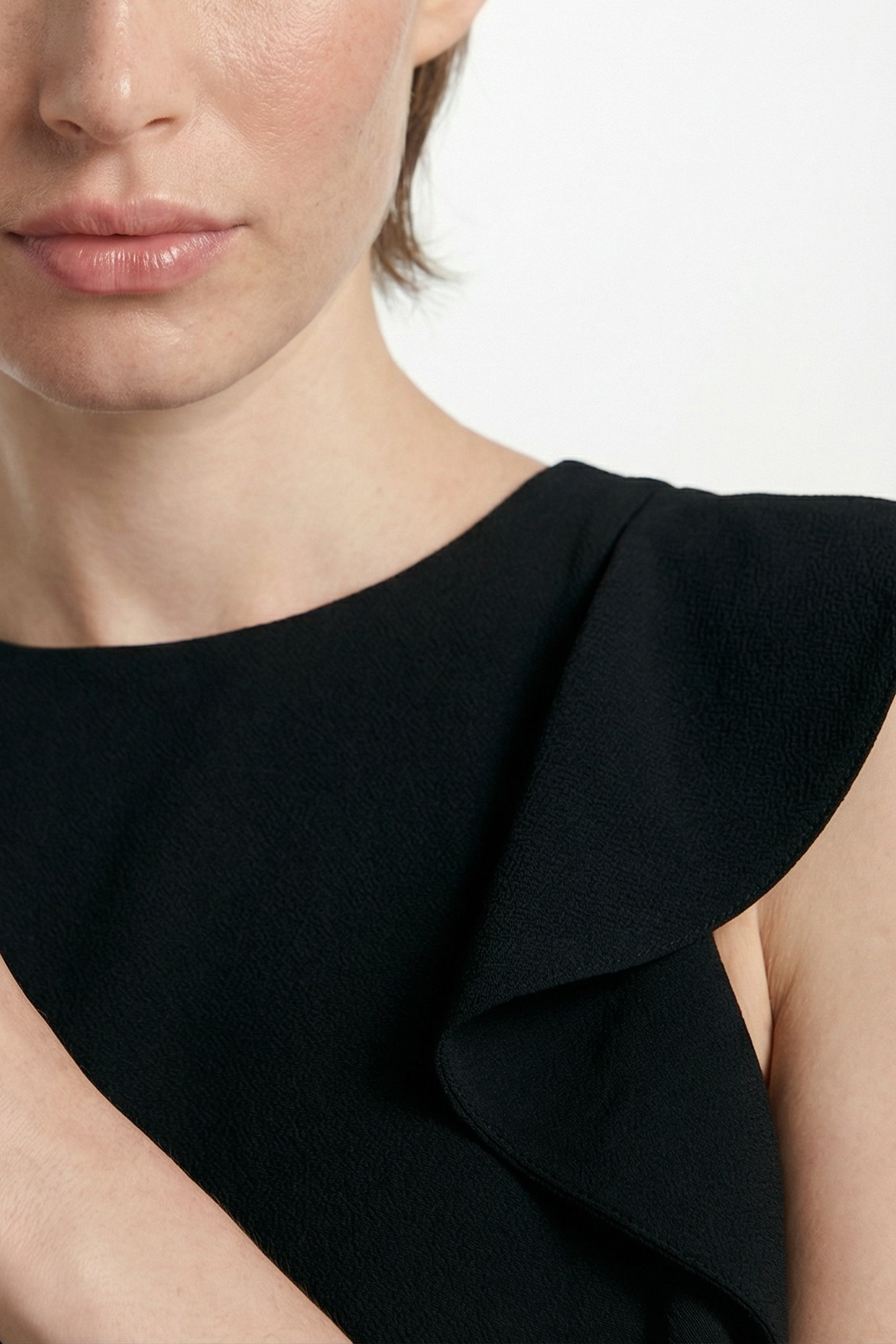 Close-up of black dress with ruffle shoulder detail, worn by model.