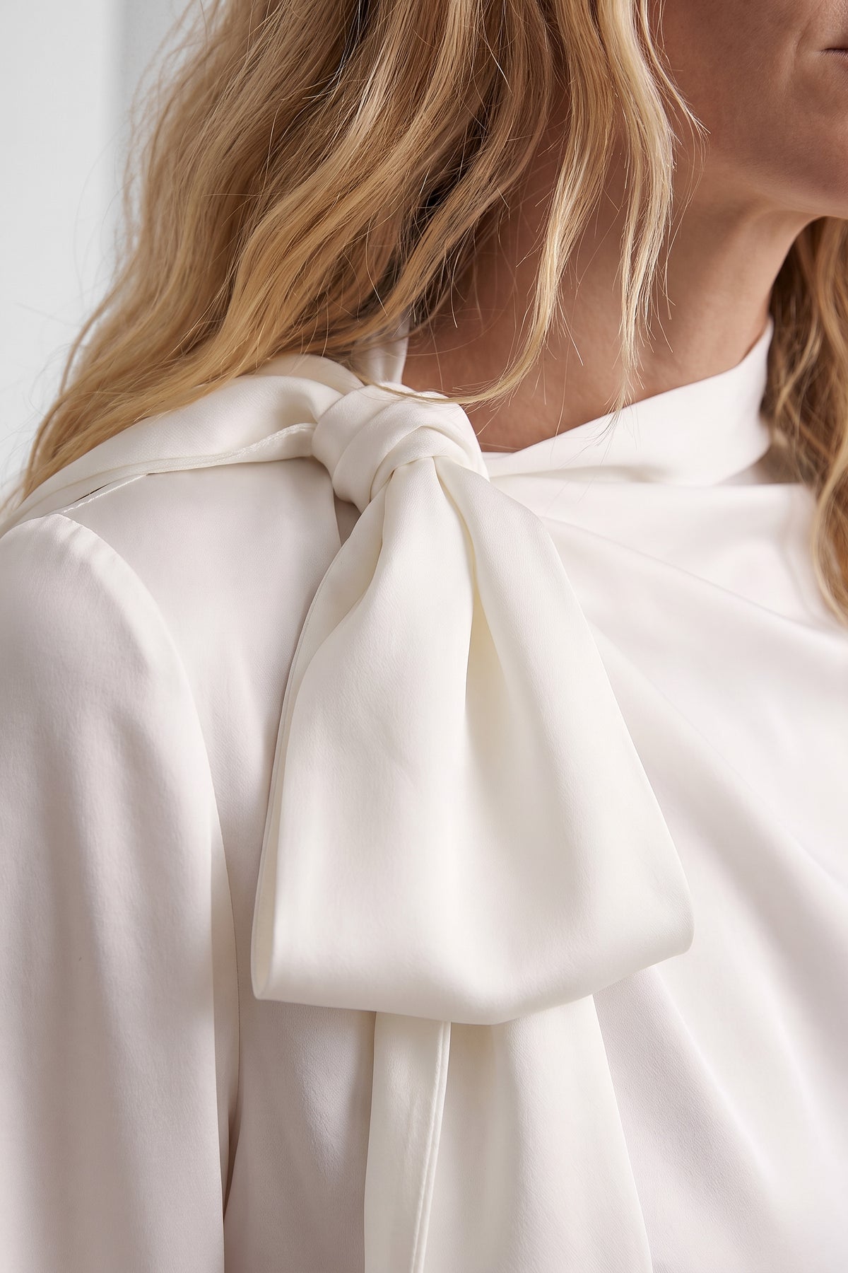 Close-up of ivory bow tie on blouse shoulder, with model's hair partially visible.