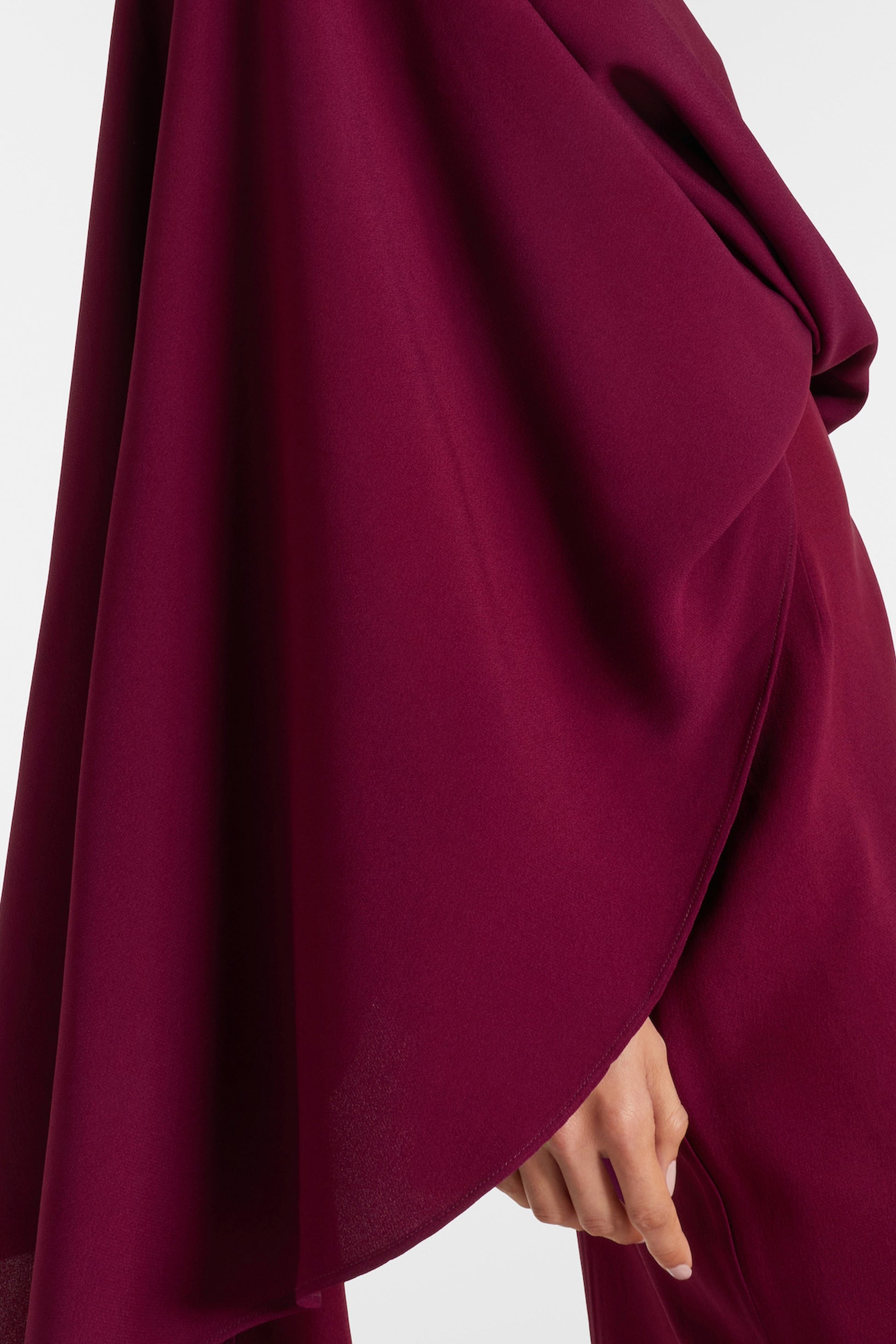 Close-up of burgundy draped slit gown on model's hand, showcasing elegant fabric details.