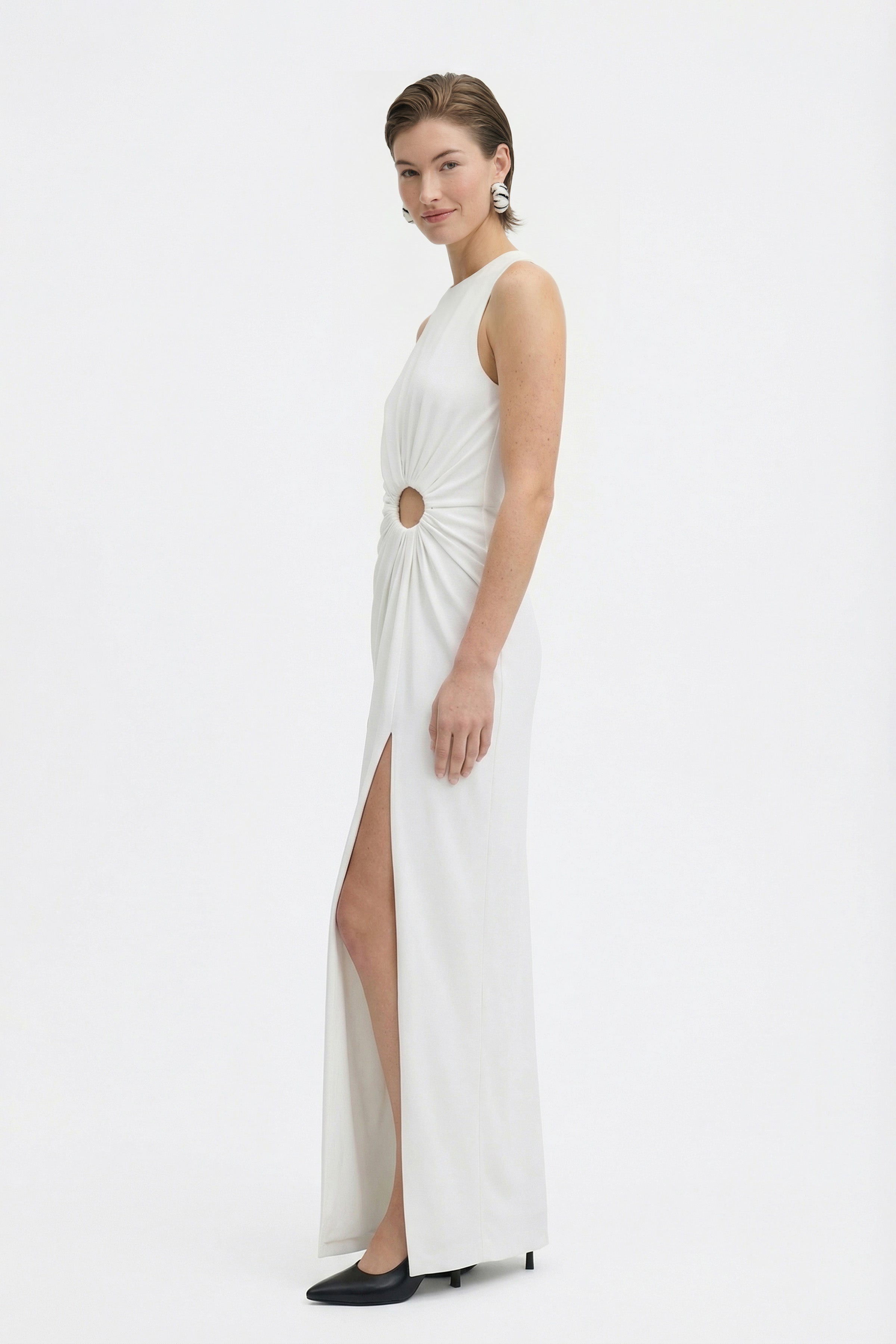Model wearing white cut-out slit gown, side view, showing ring detail and slit.