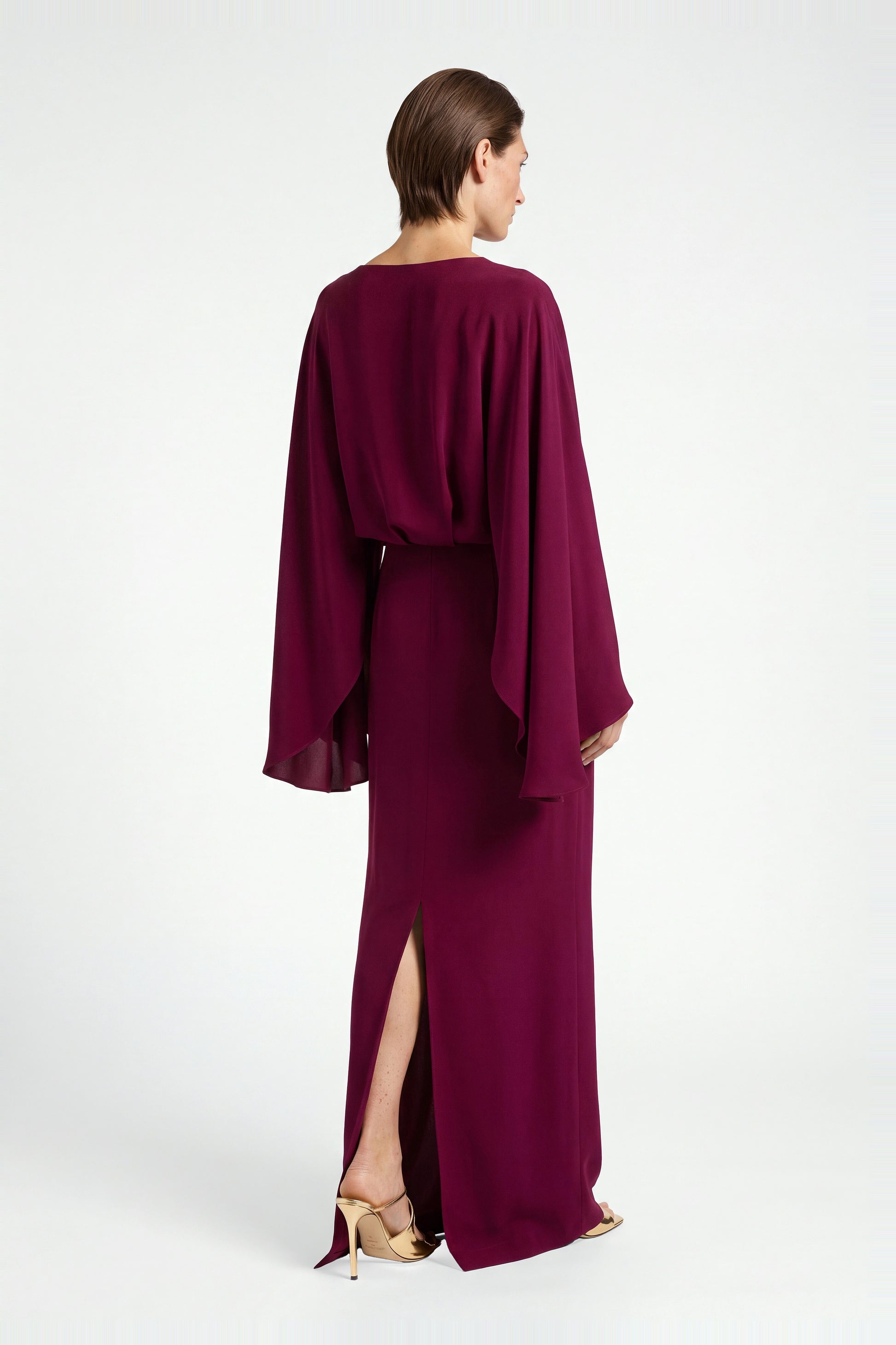 Back view of burgundy draped gown with slit, model wearing gold heels.