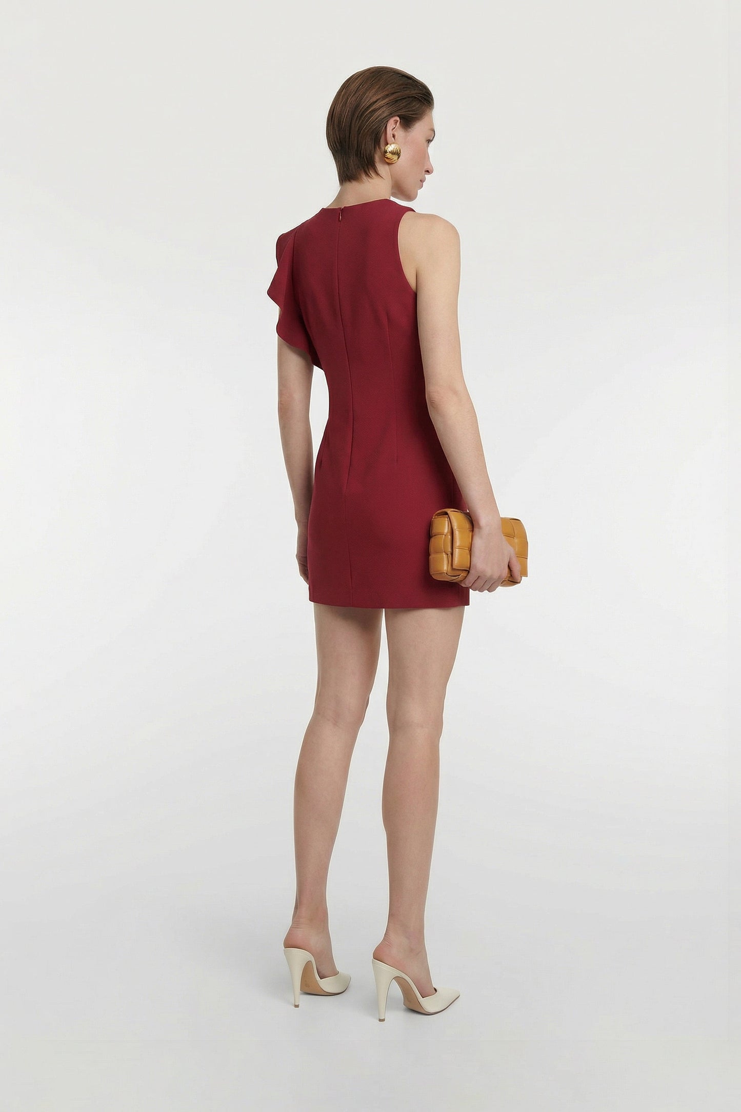 Back view of model wearing ruffled scarlet mini dress, with beige heels and clutch.