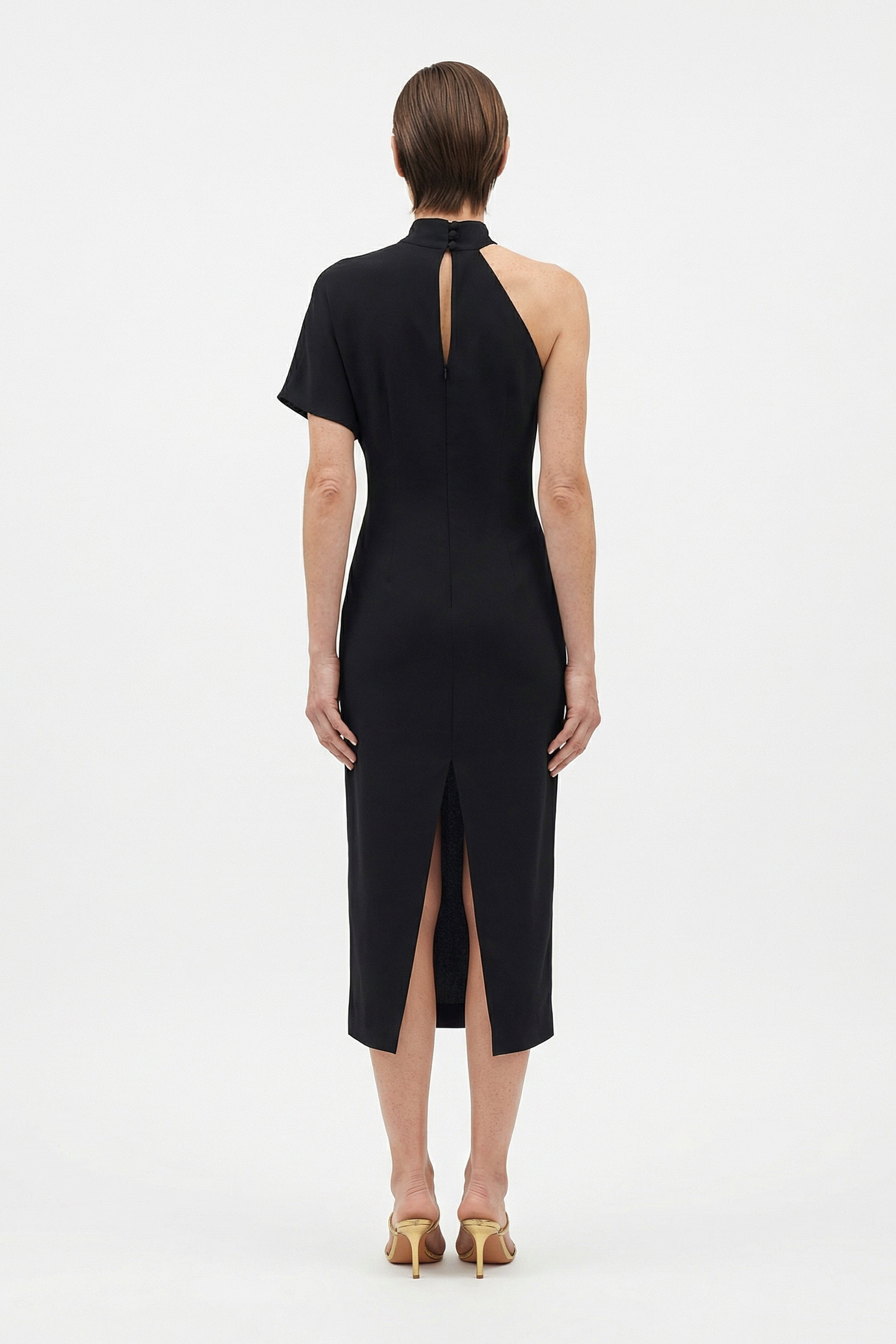 Back view of asymmetrical black midi dress with slit and one-shoulder design.