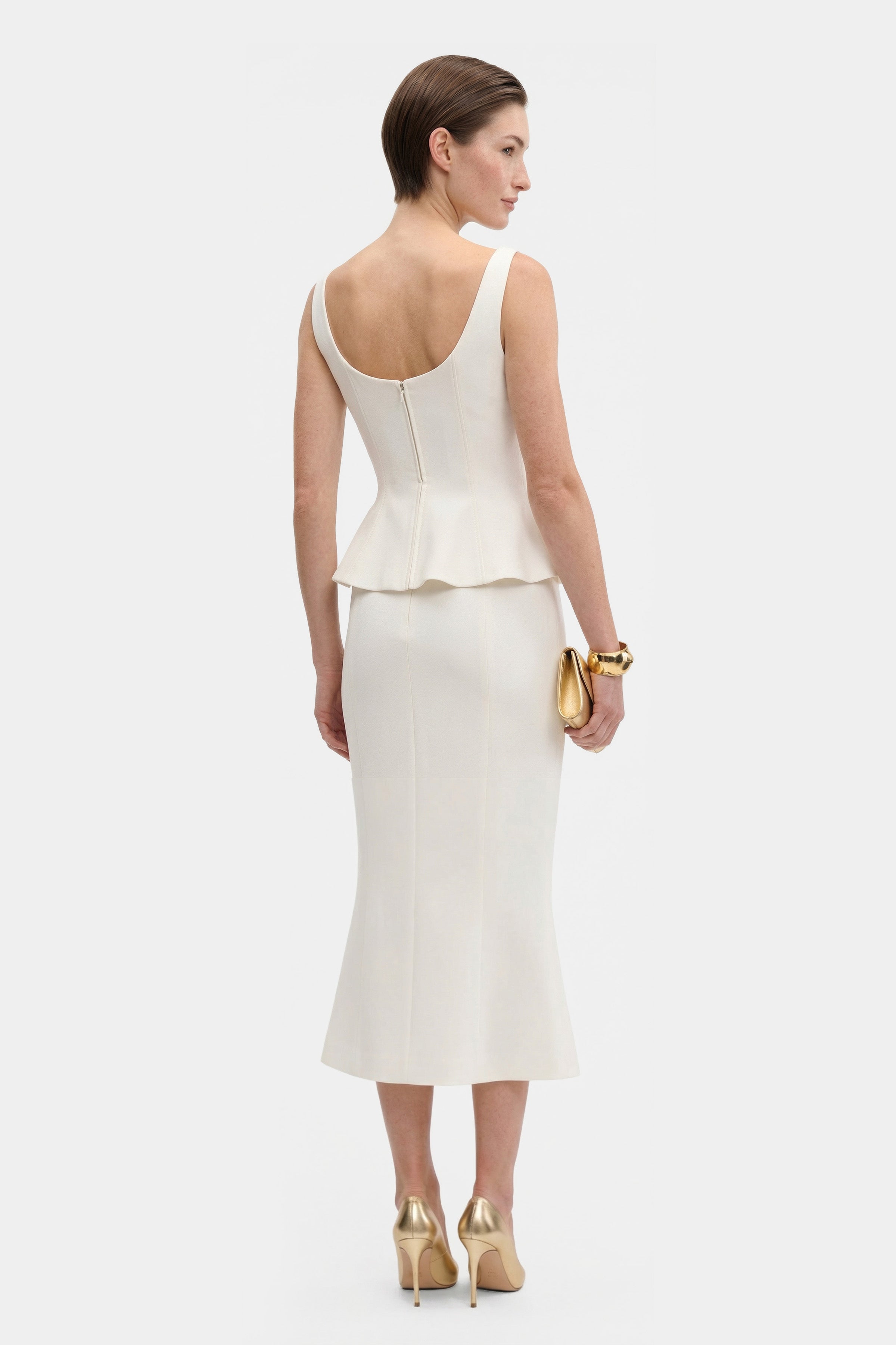 Back view of ivory peplum top on model, paired with matching skirt.