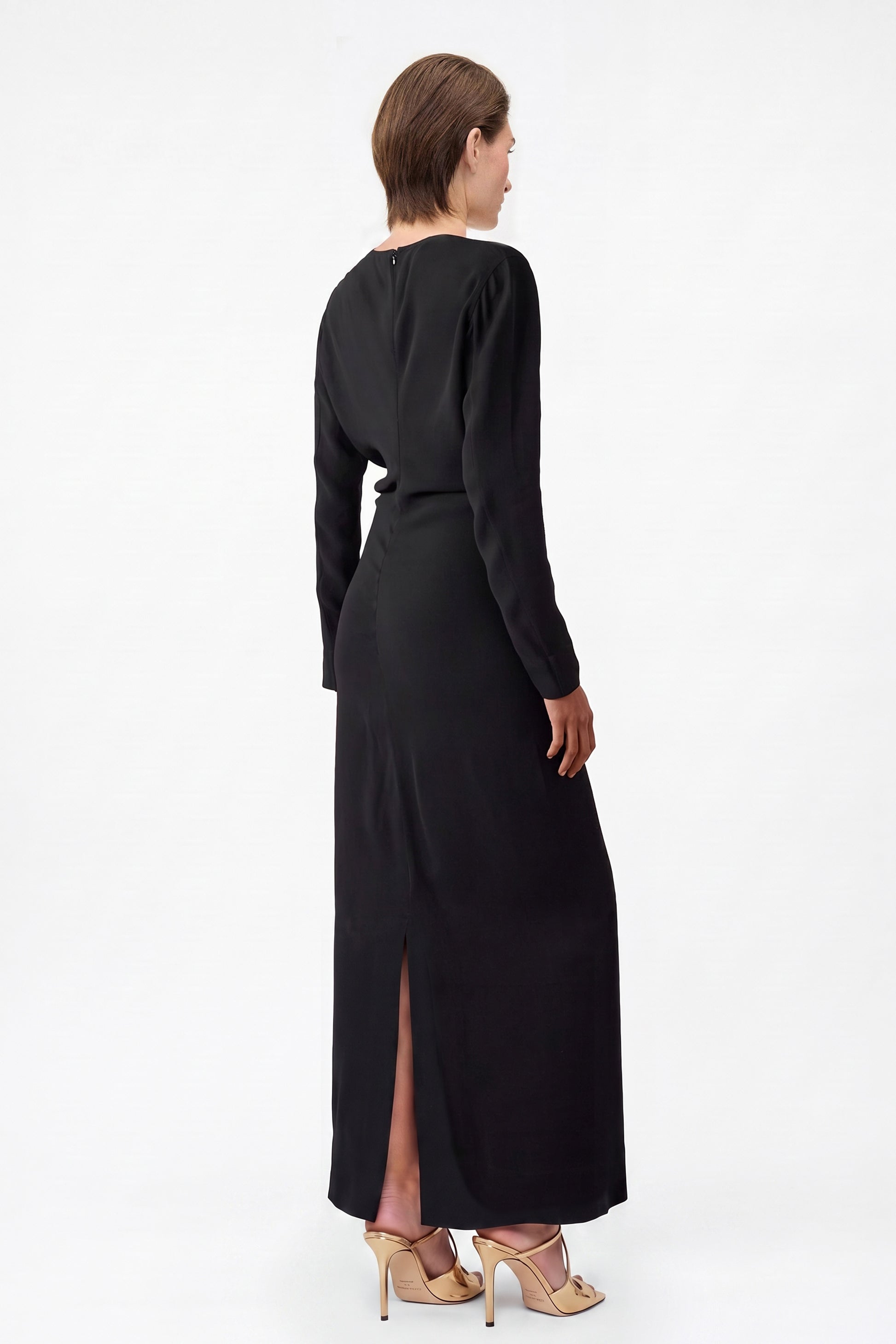 Back view of black long sleeve maxi dress with slit, model in heels.