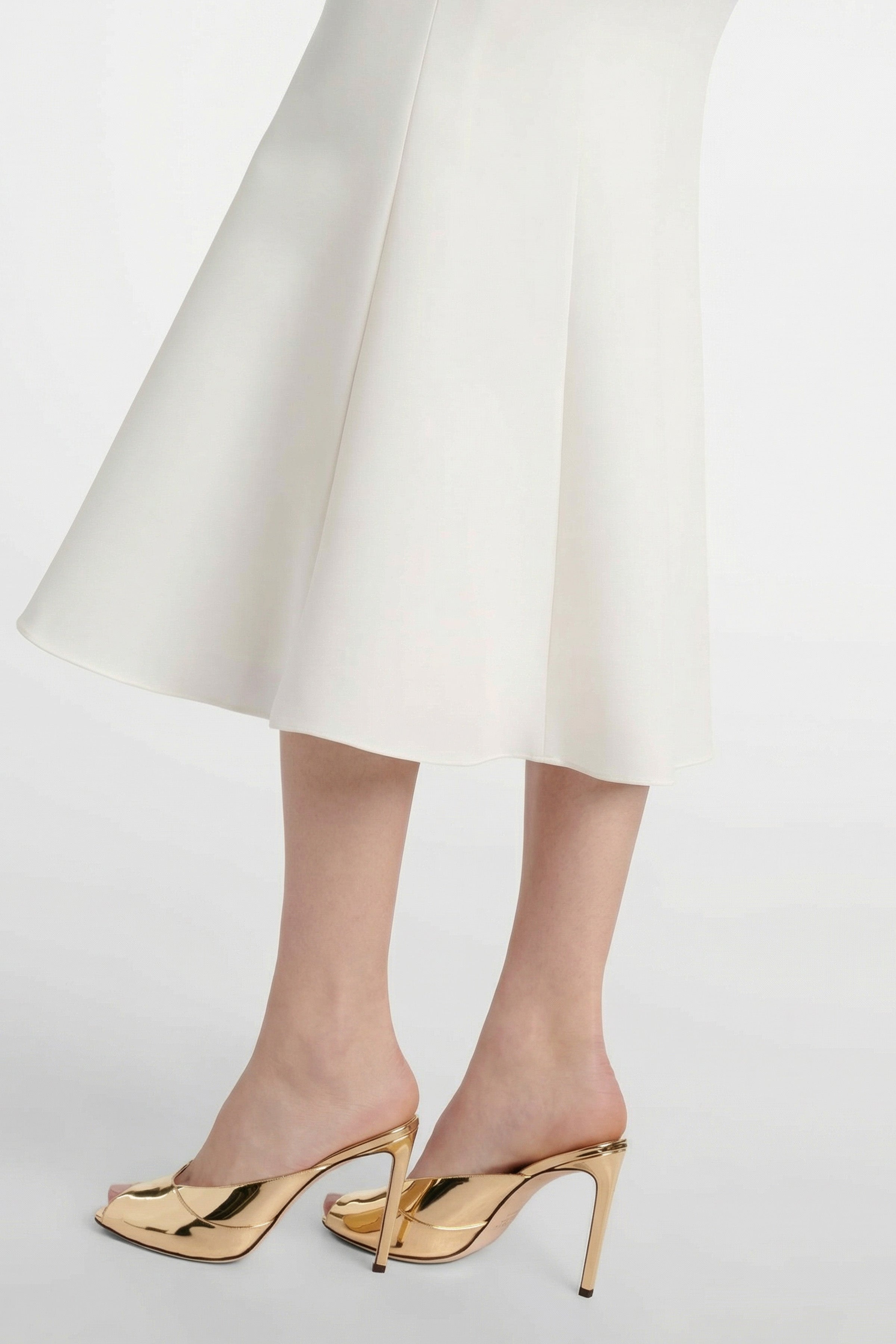 Close-up of Ivory Elegance Midi skirt hem and model's gold heels.