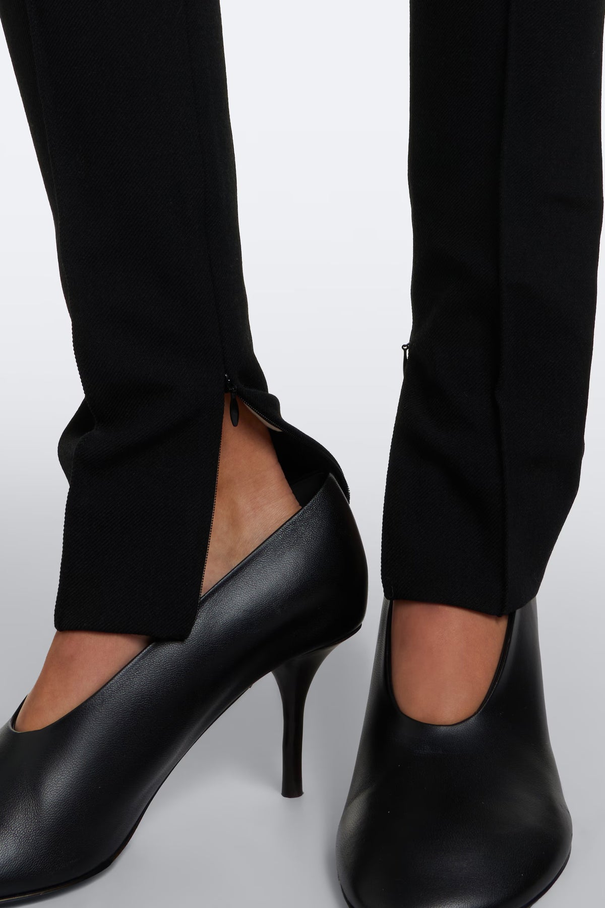 Close-up of tailored black suit pants with zipper detail and black high heels.