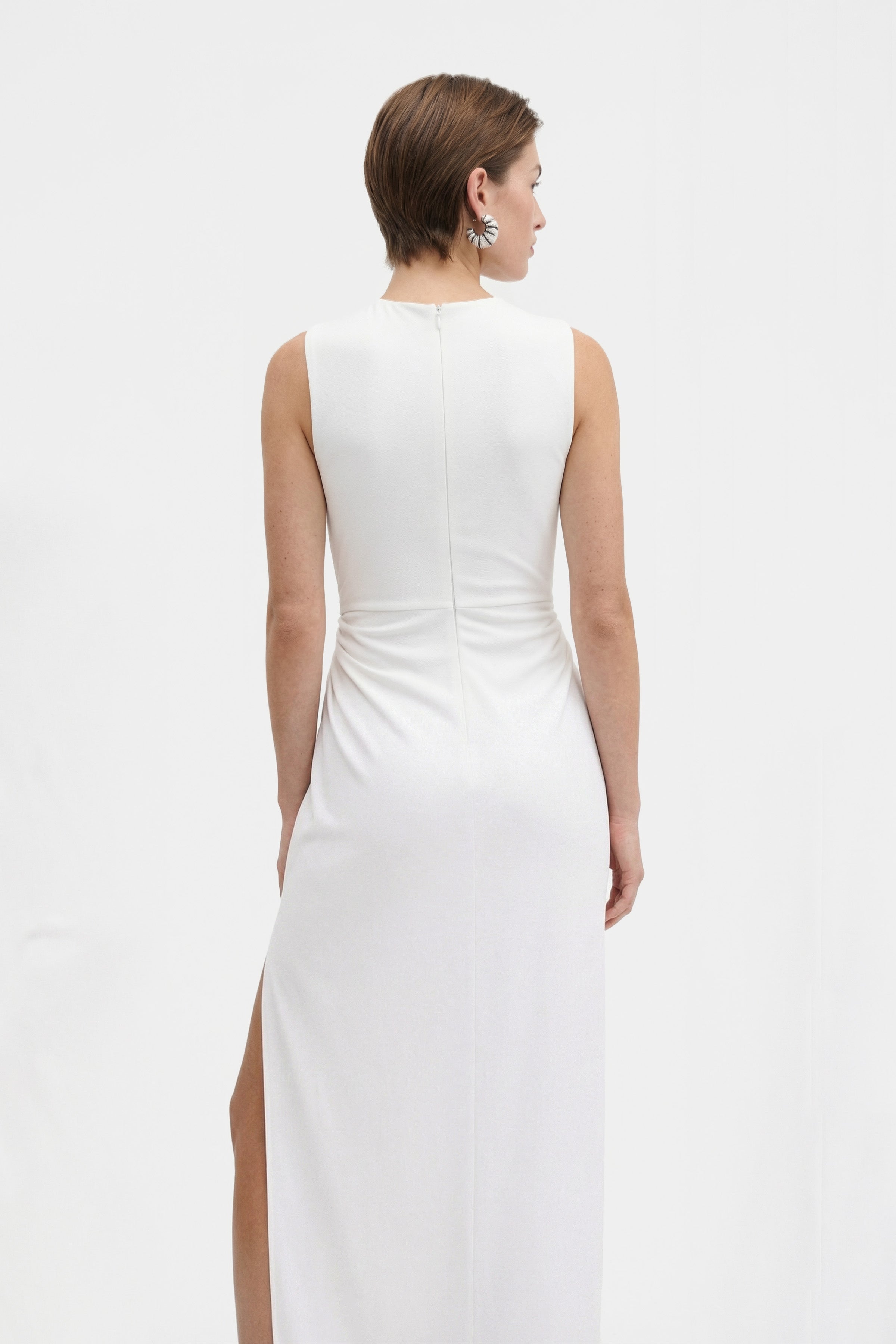 Back view of a white cut-out slit gown on a model with short hair.