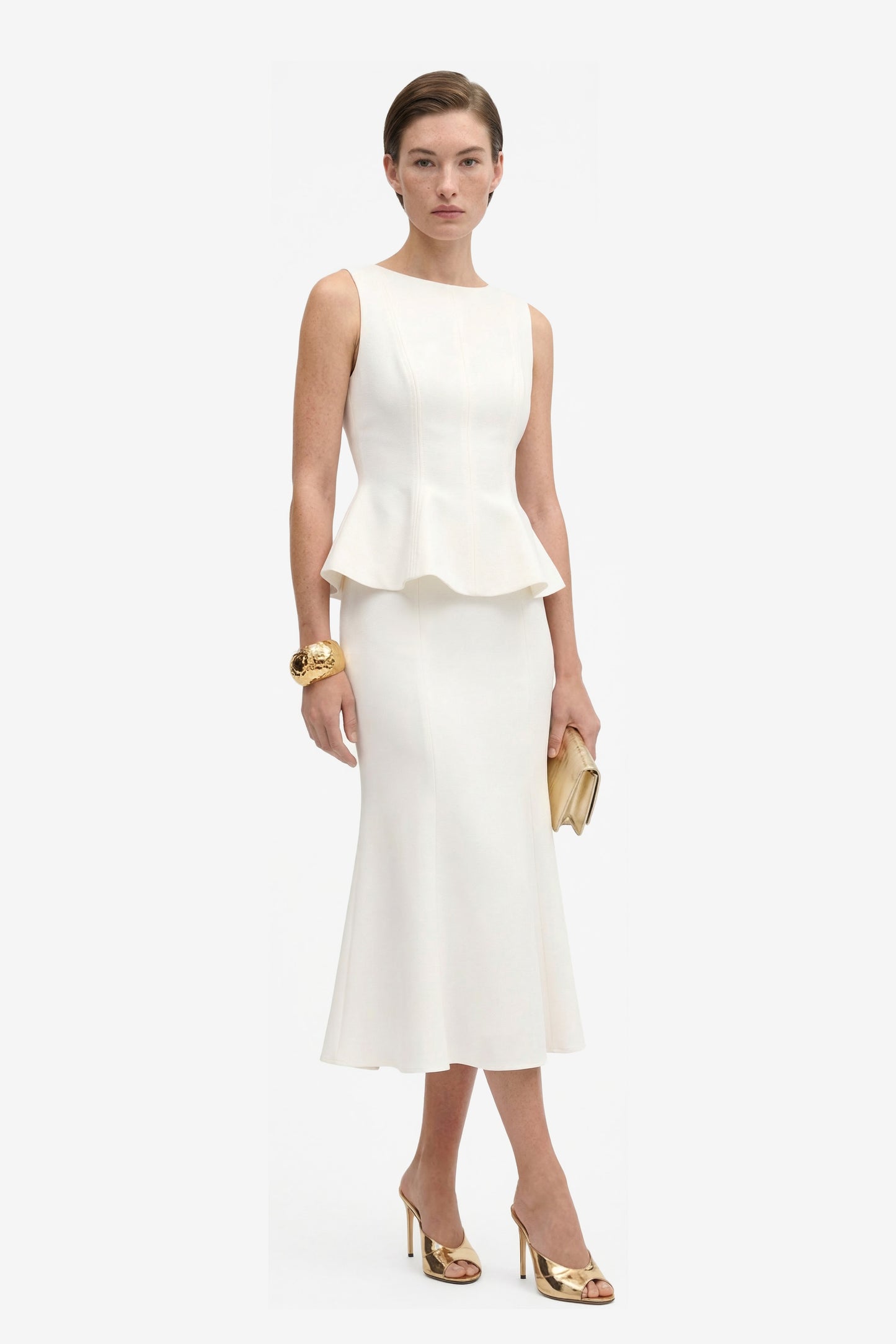 Model wearing Ivory Elegance Midi skirt, peplum detail, holding clutch, gold heels.