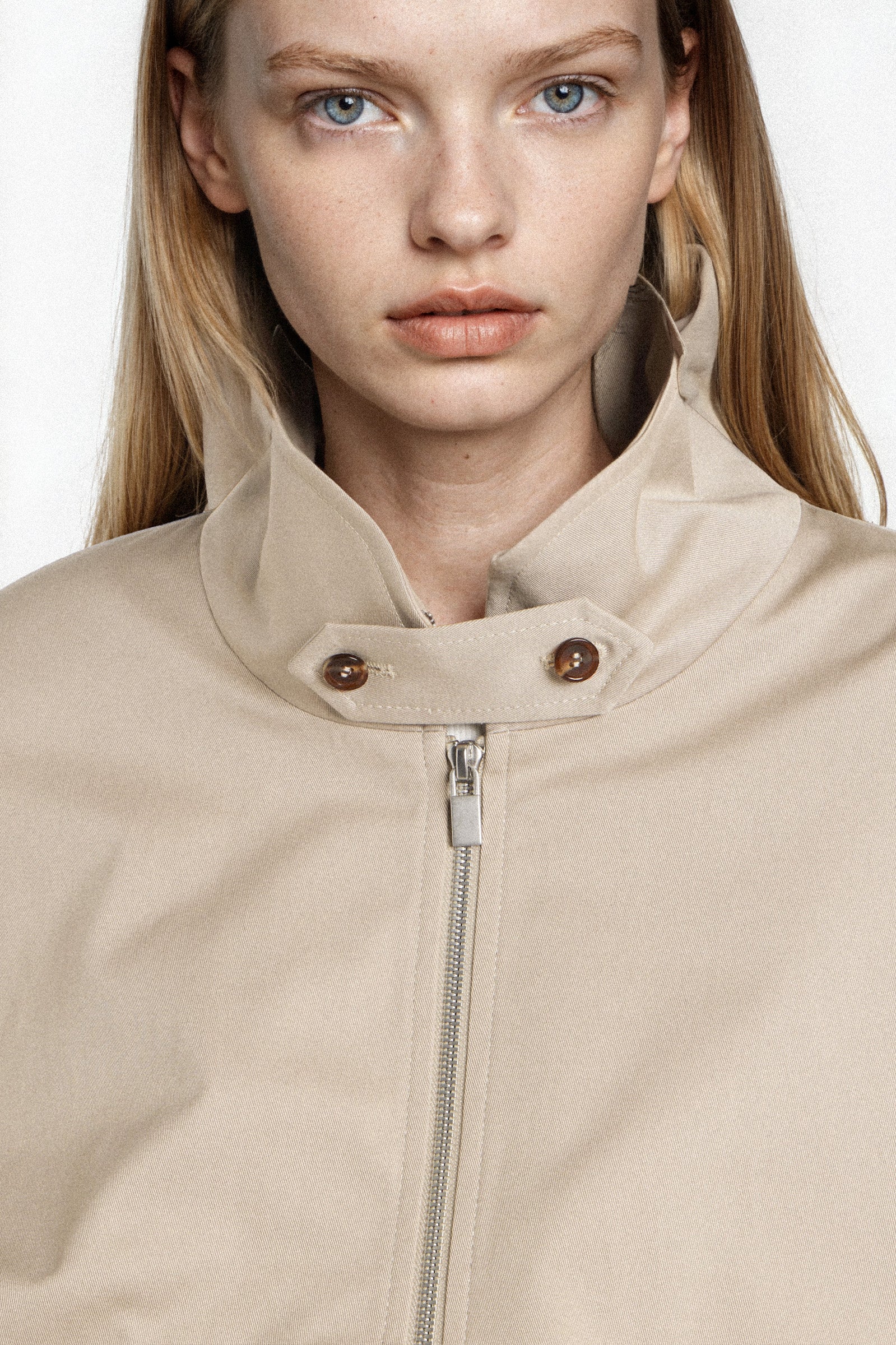 Close-up of high collar with button fastening on beige bomber jacket